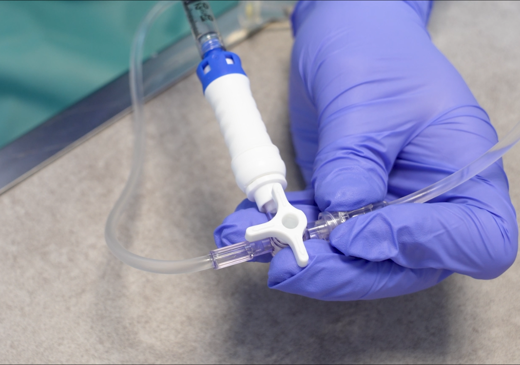 Des mains gantées tiennent un instrument médical relié à une tubulure, le tout recouvert d'un champ opératoire.