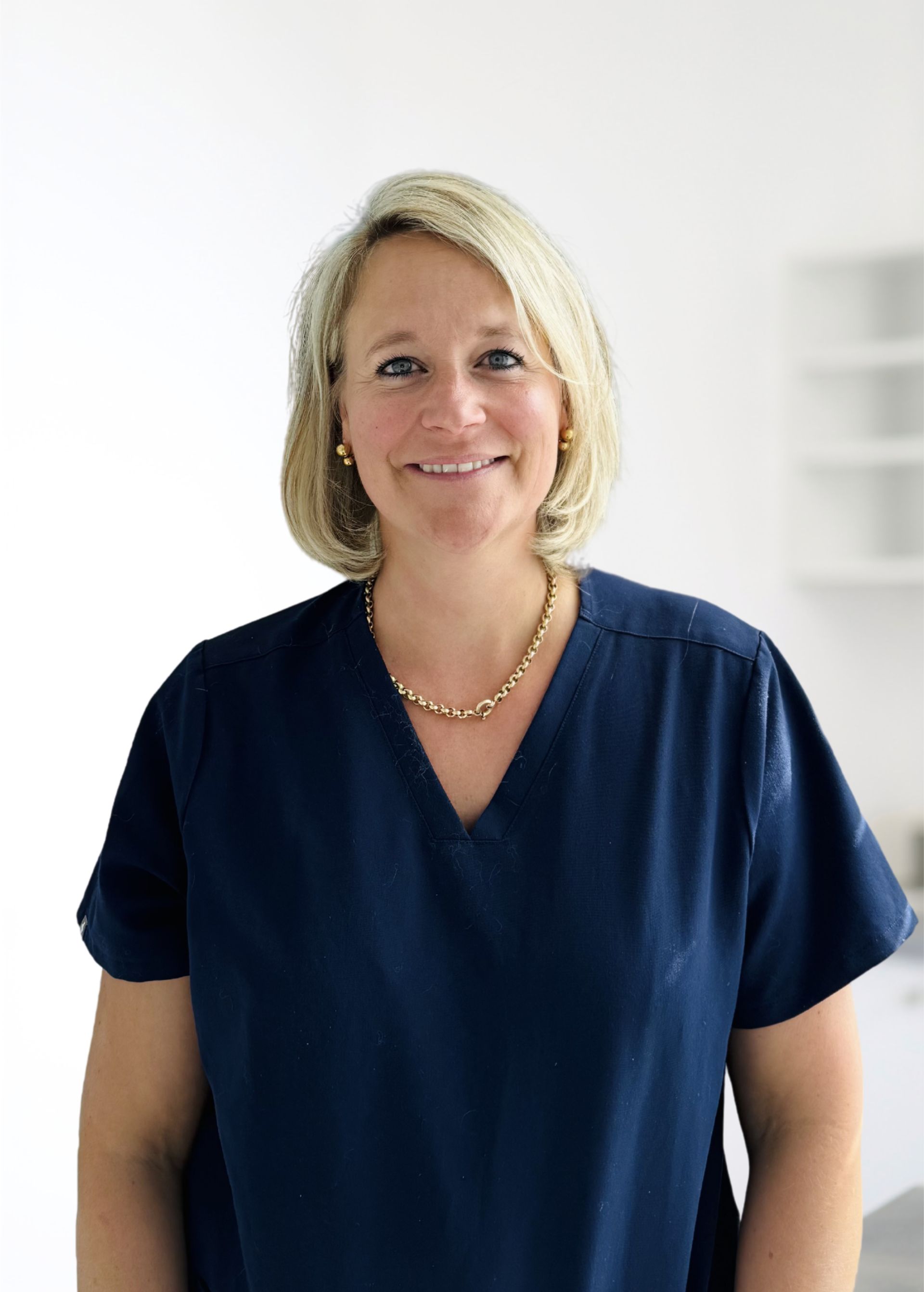 Femme souriante en chemisier bleu marine et collier doré se détachant sur un fond blanc