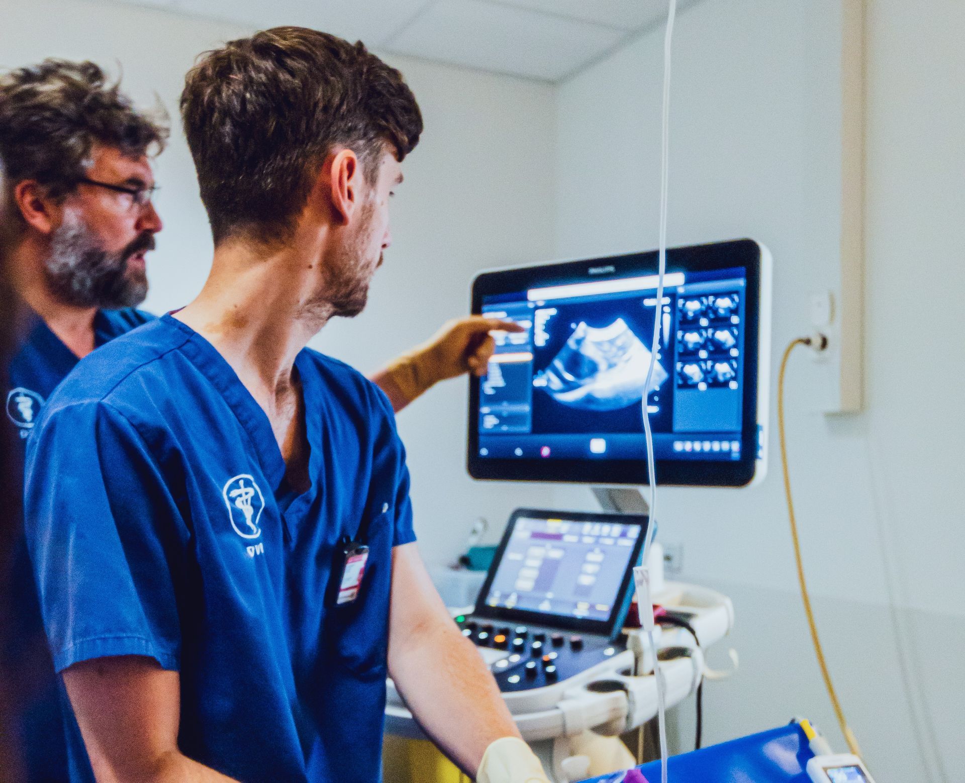 Deux cliniciens examinent une échographie sur un écran médical dans une salle d'examen d'hôpital.
