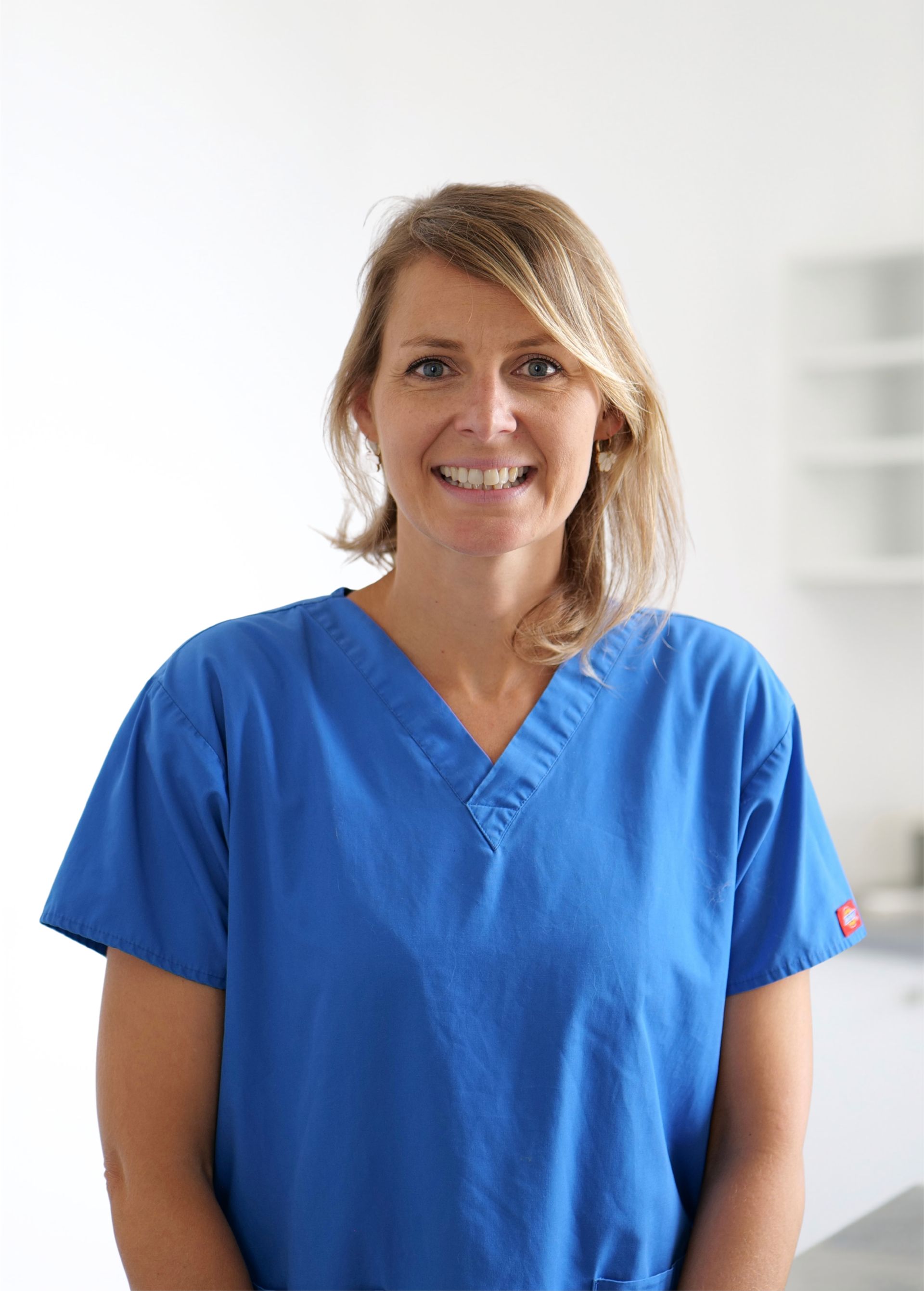 Femme en blouse médicale bleue souriant dans une pièce lumineuse