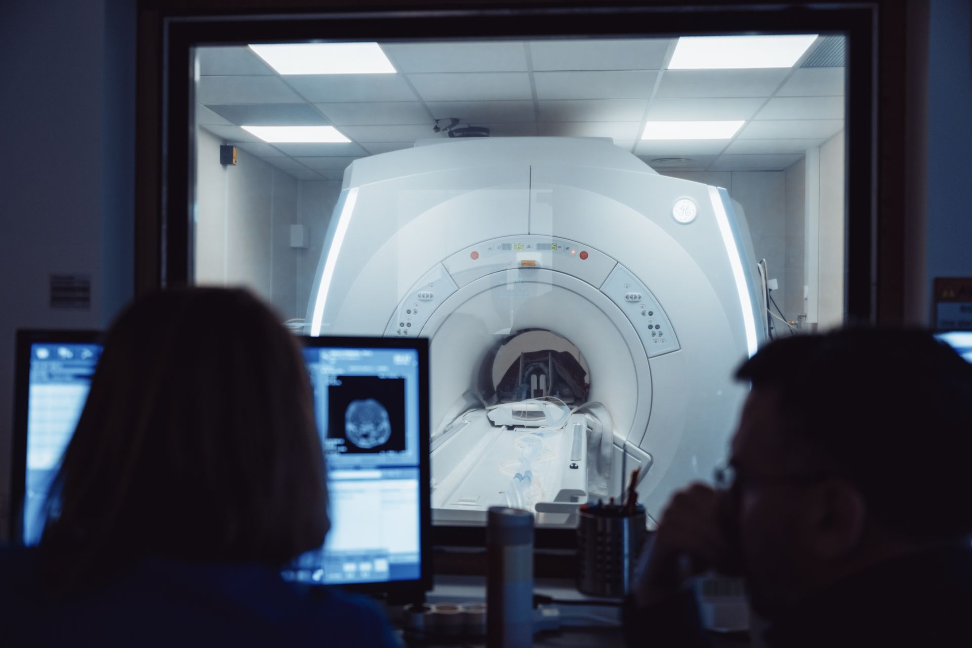Des techniciens observent un grand scanner médical à travers une fenêtre de salle de contrôle