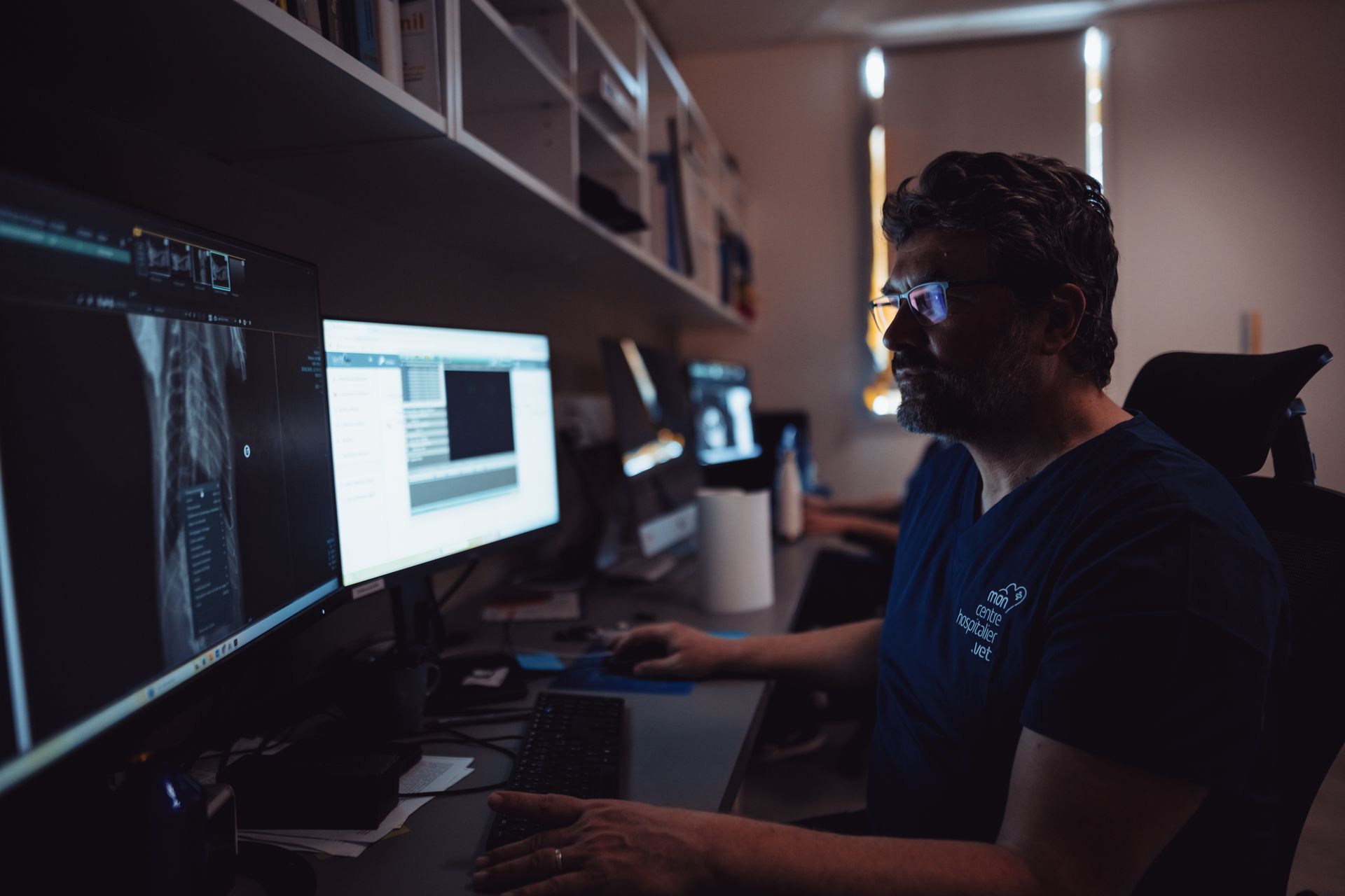 Une personne travaillant sur un ordinateur dans un bureau faiblement éclairé, avec plusieurs écrans et du code affiché à l'écran.