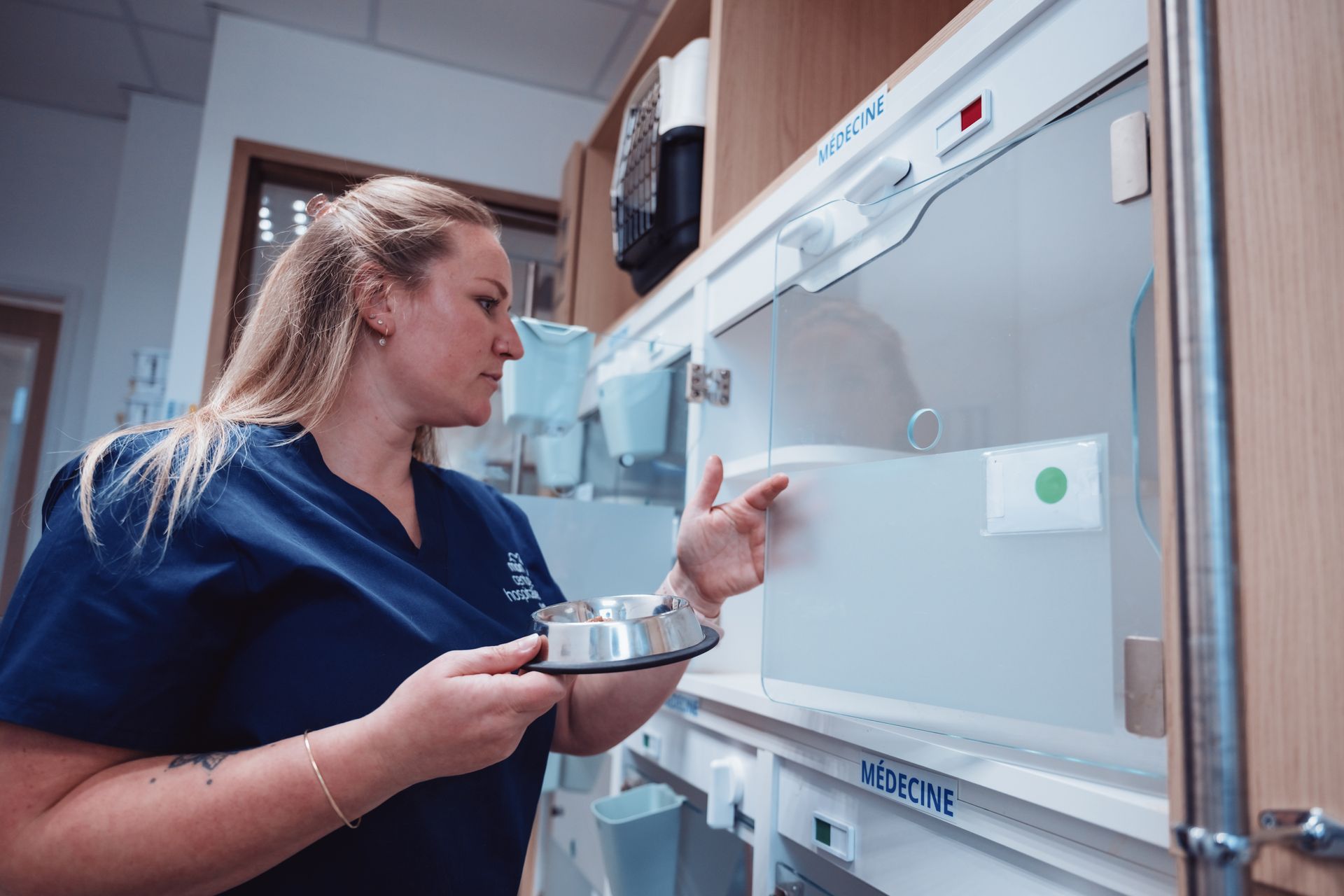 Technicien en blouse bleue inspectant une machine de laboratoire et tenant un plateau dans un laboratoire clinique.