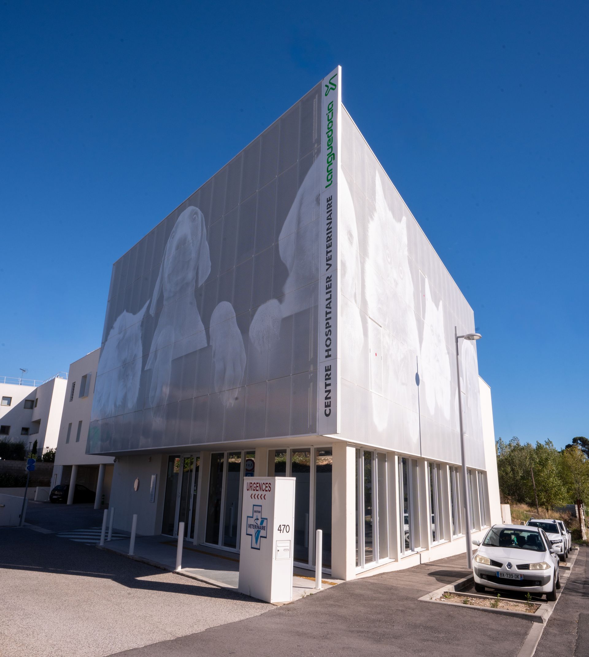 Immeuble blanc moderne à façade à motifs, situé dans une rue ensoleillée sous un ciel bleu azur.