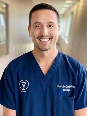 Une vétérinaire en blouse bleue sourit dans le couloir d'une clinique.