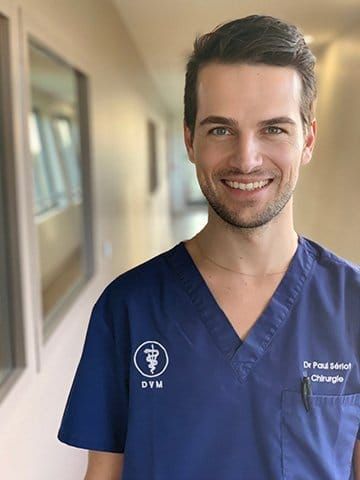 Une soignante souriante en blouse bleu marine se tient dans un couloir d'hôpital