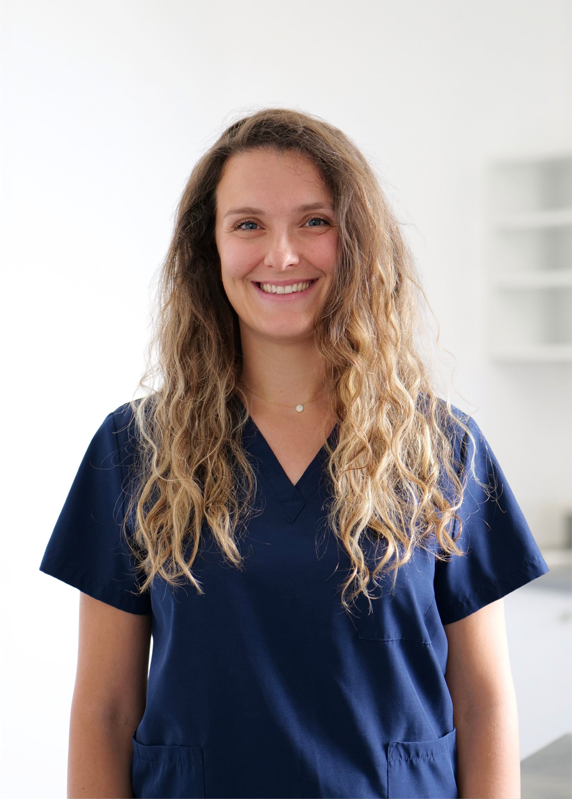 Personne souriante en blouse médicale bleu marine se détachant sur un fond blanc éclatant