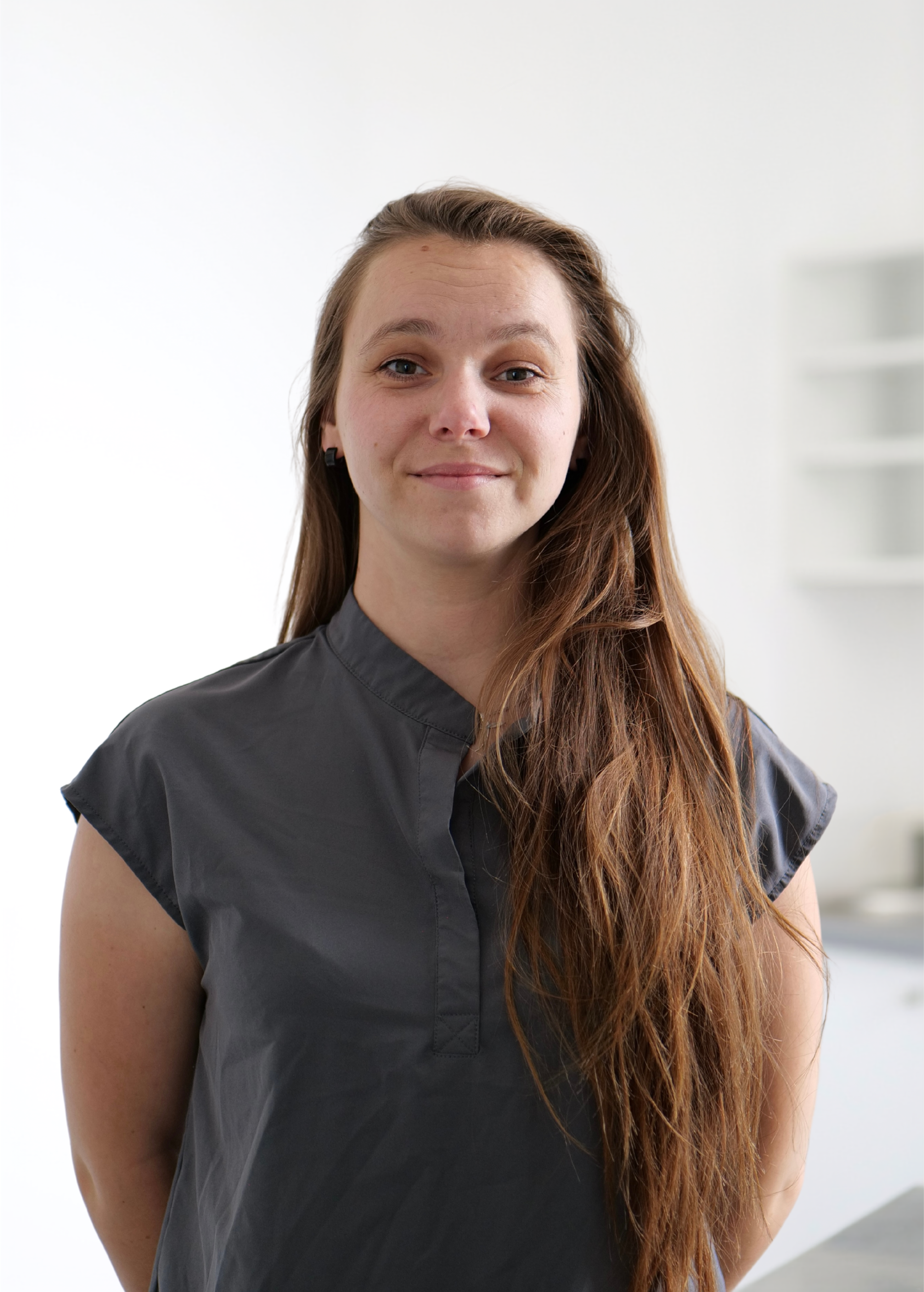 Personne debout à l'intérieur, sur fond clair, portant une chemise gris foncé et arborant un léger sourire.