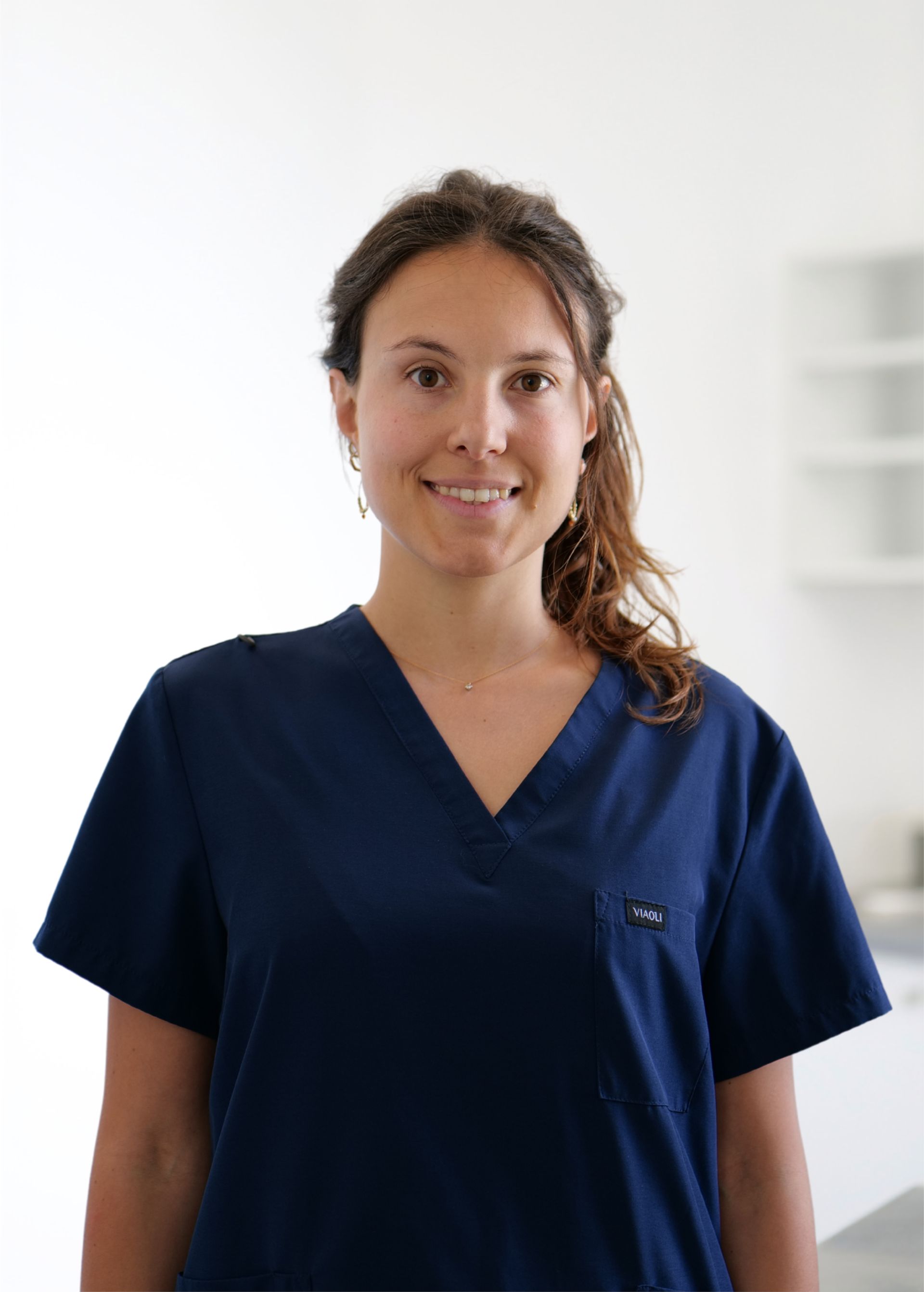 Une soignante en blouse bleu marine sourit dans un cadre clinique lumineux