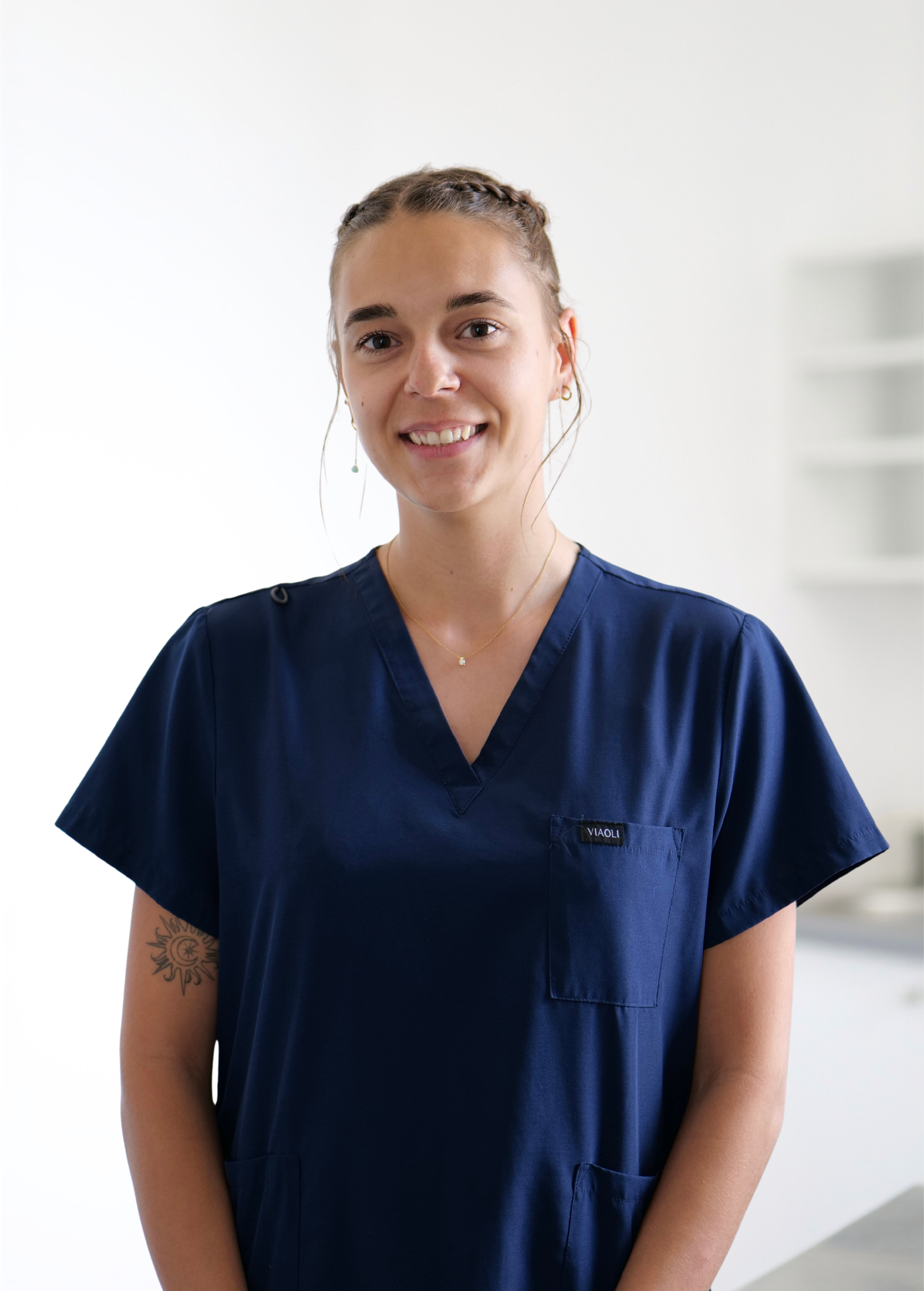 Personne en blouse médicale bleu marine souriant dans un intérieur lumineux