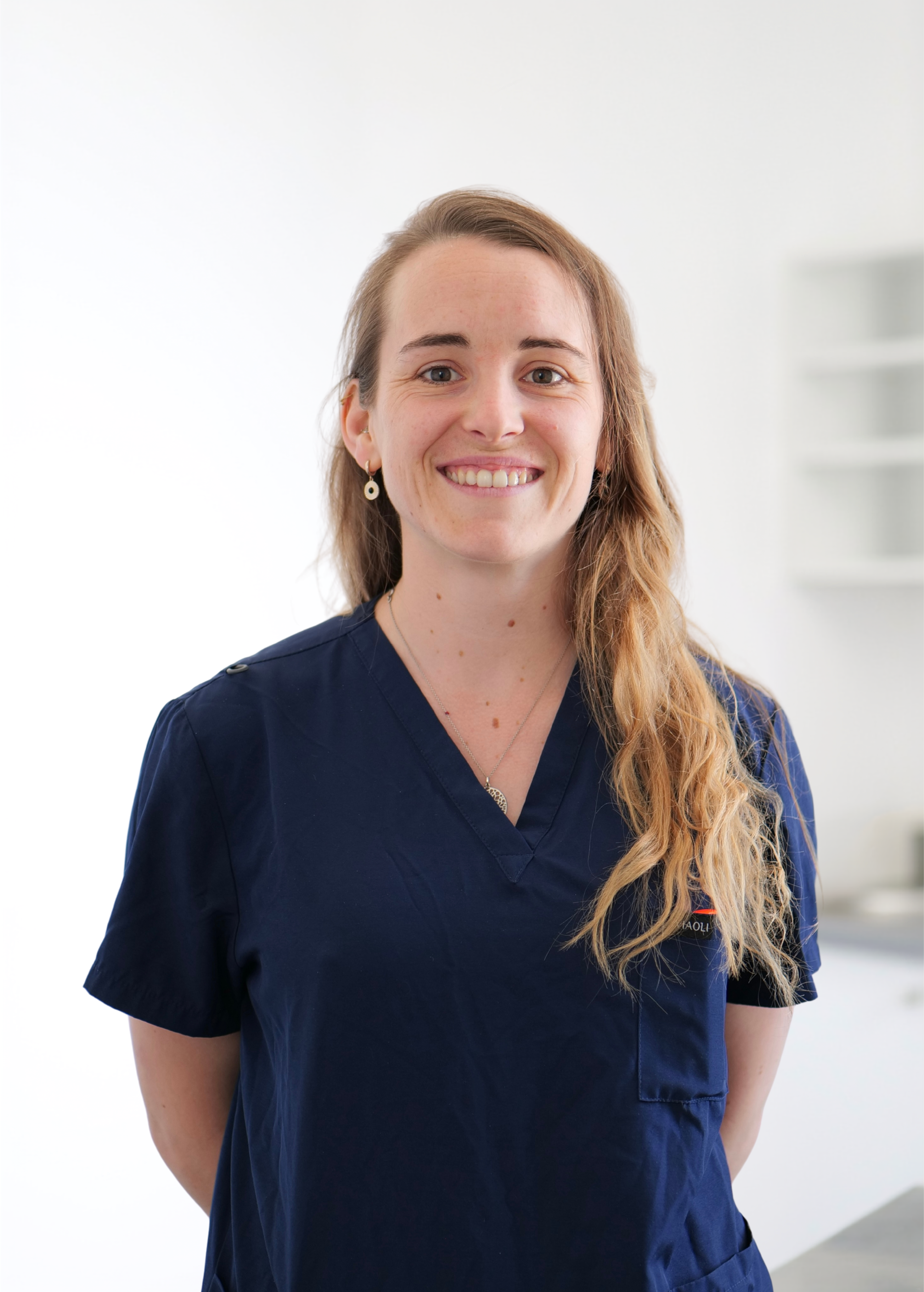 Personne souriante en blouse médicale bleu marine se détachant sur un fond blanc éclatant