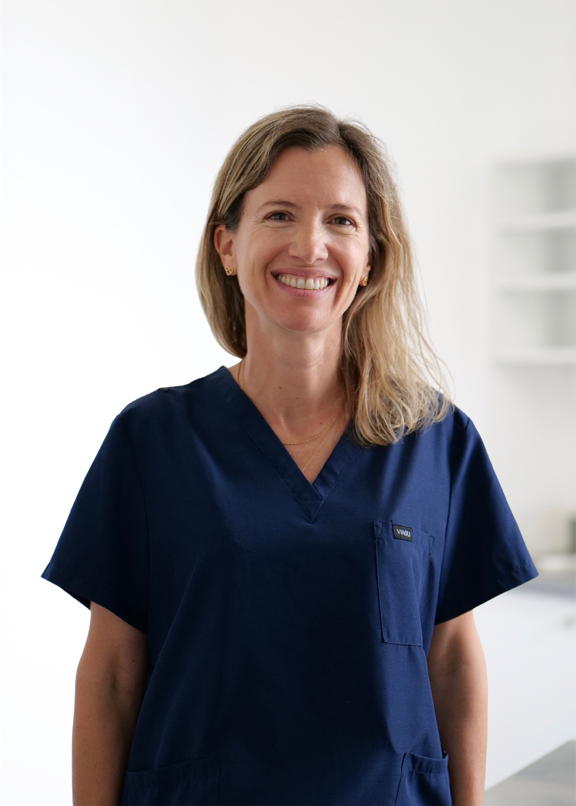Infirmière souriante en blouse bleu marine, debout à l'intérieur sur fond blanc