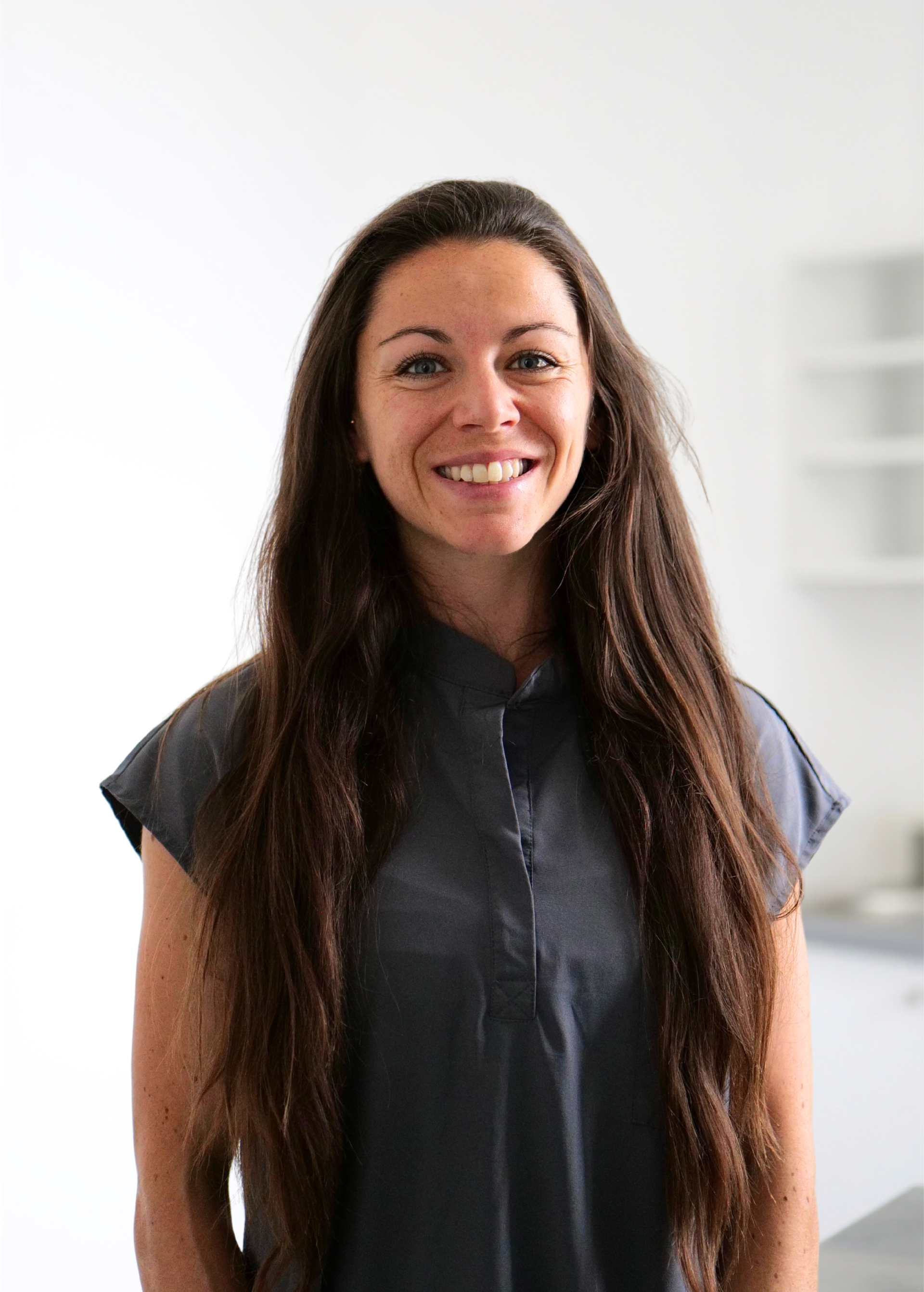 Femme souriante aux longs cheveux noirs, debout à l'intérieur sur un fond blanc éclatant