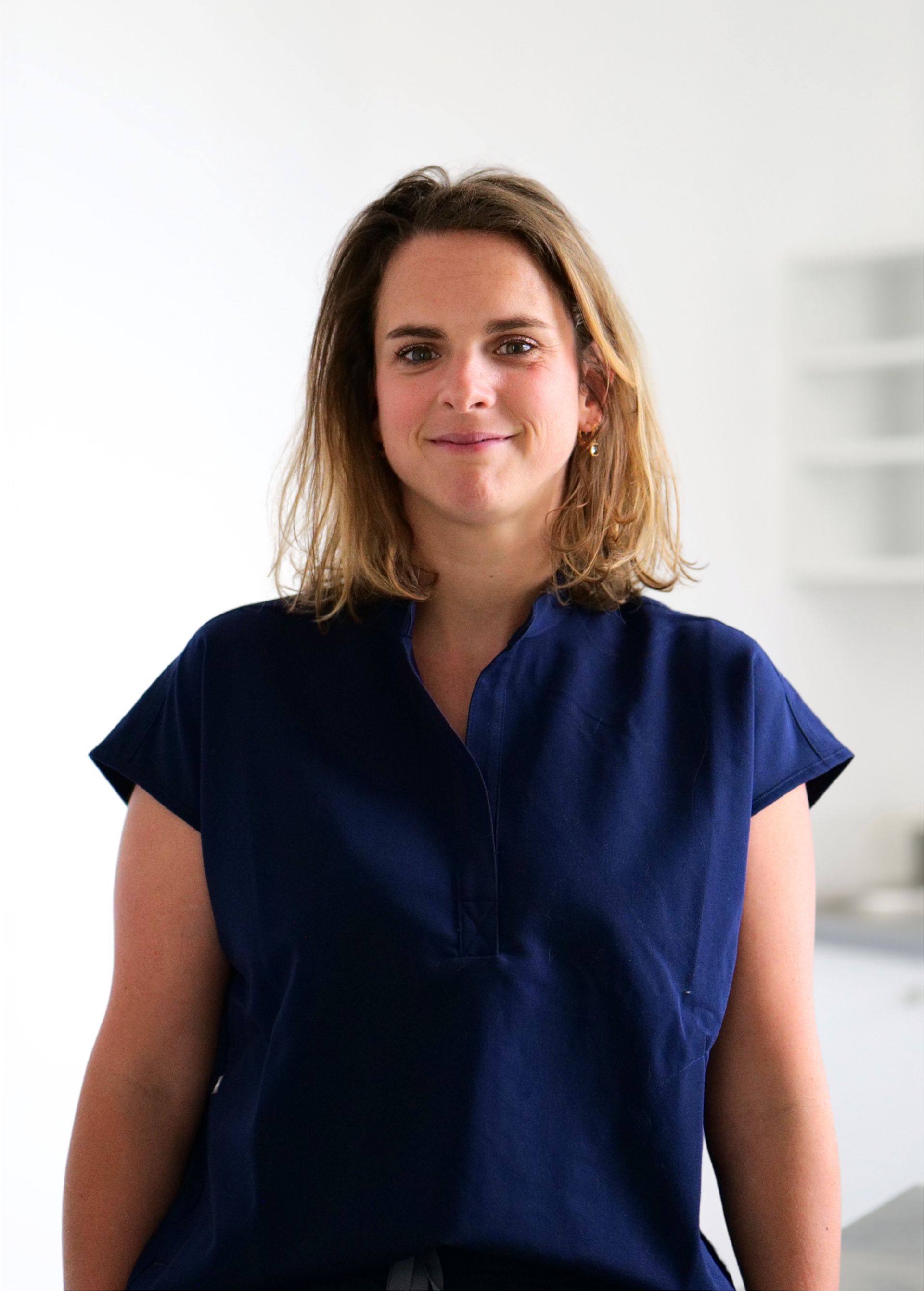 Femme vêtue d'un haut bleu marine, debout à l'intérieur sur un fond blanc éclatant.
