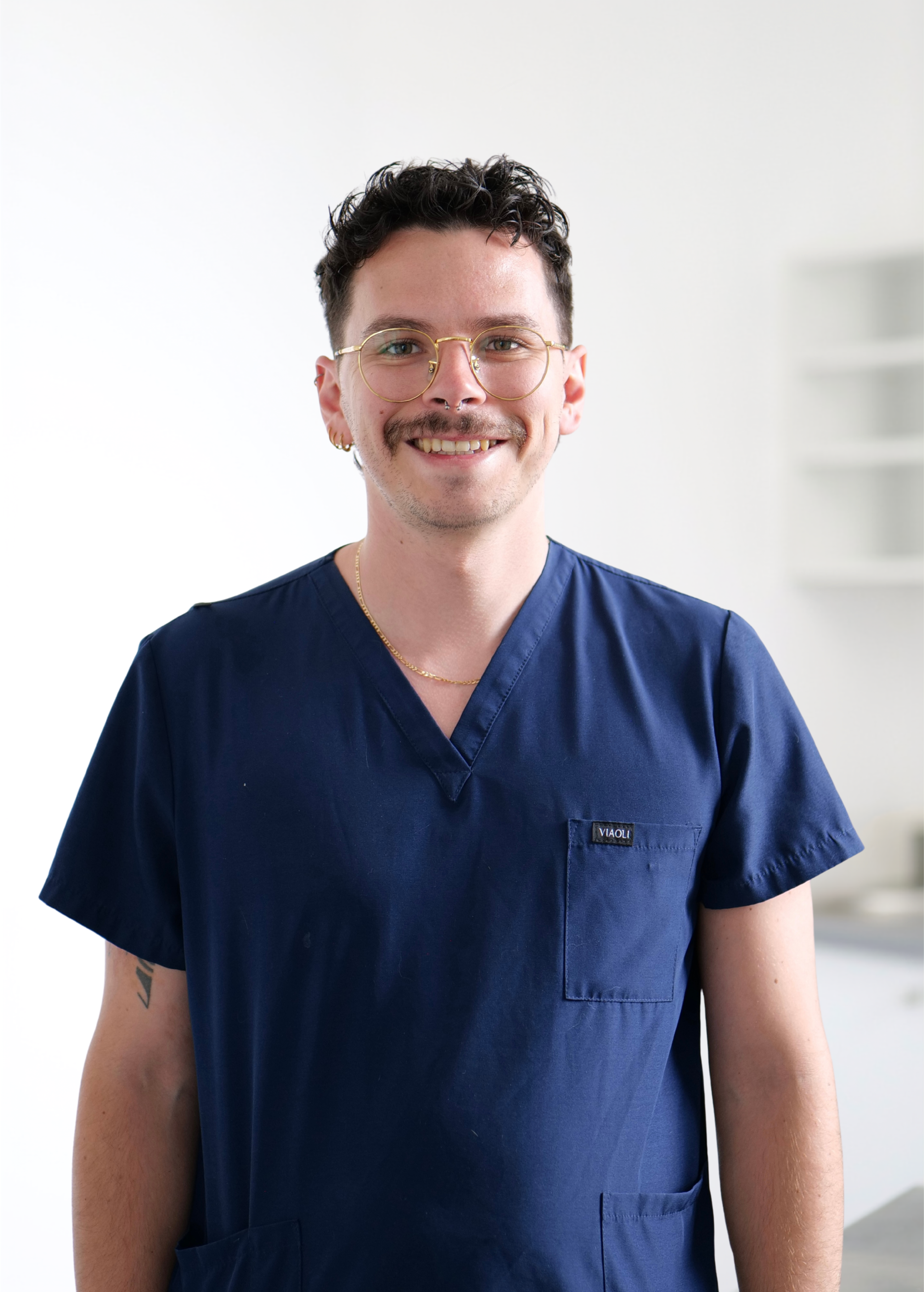 Personne souriante en blouse médicale bleu marine se détachant sur un fond blanc éclatant