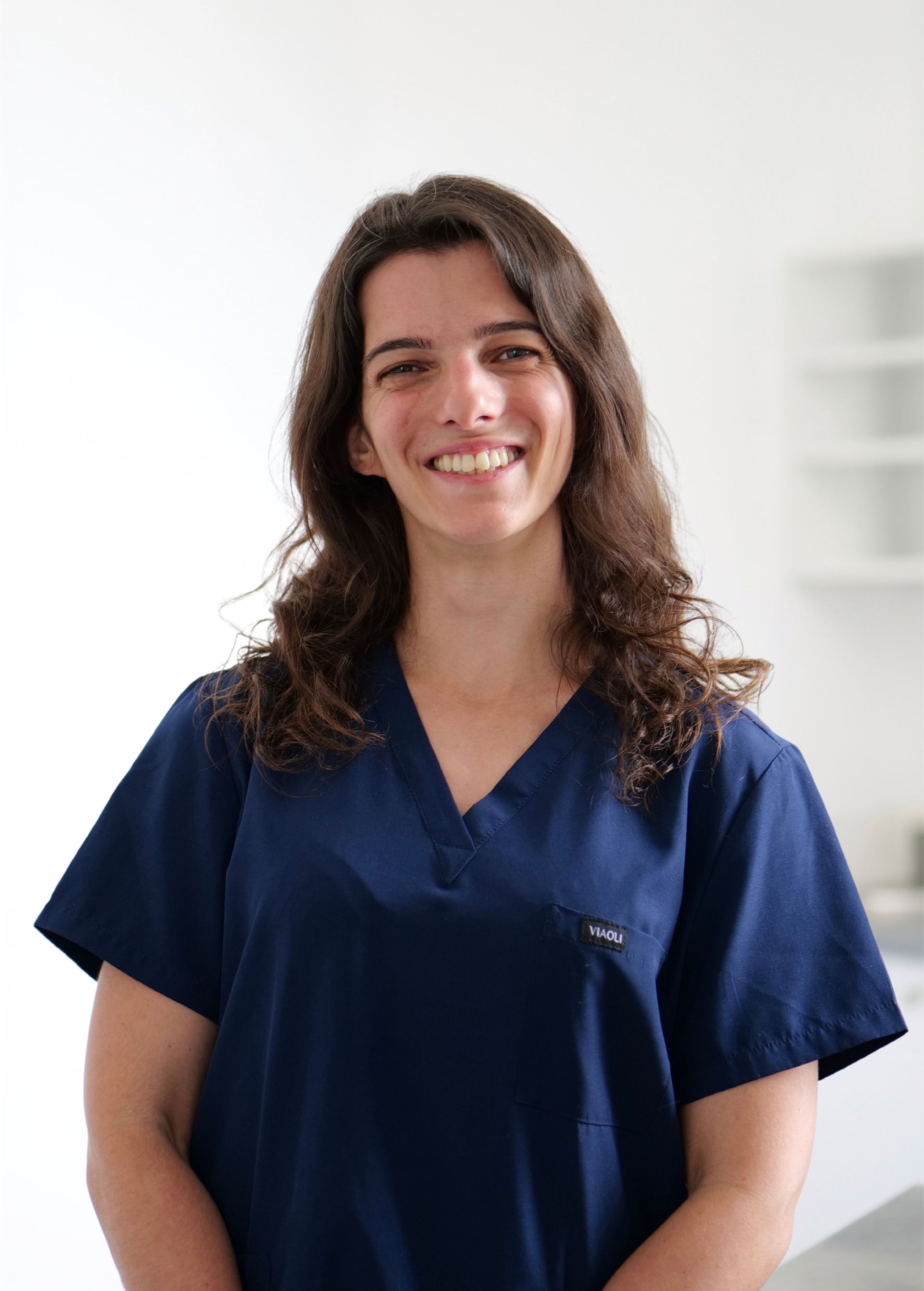 Soignante souriante en blouse bleu marine, debout à l'intérieur sur un fond blanc éclatant