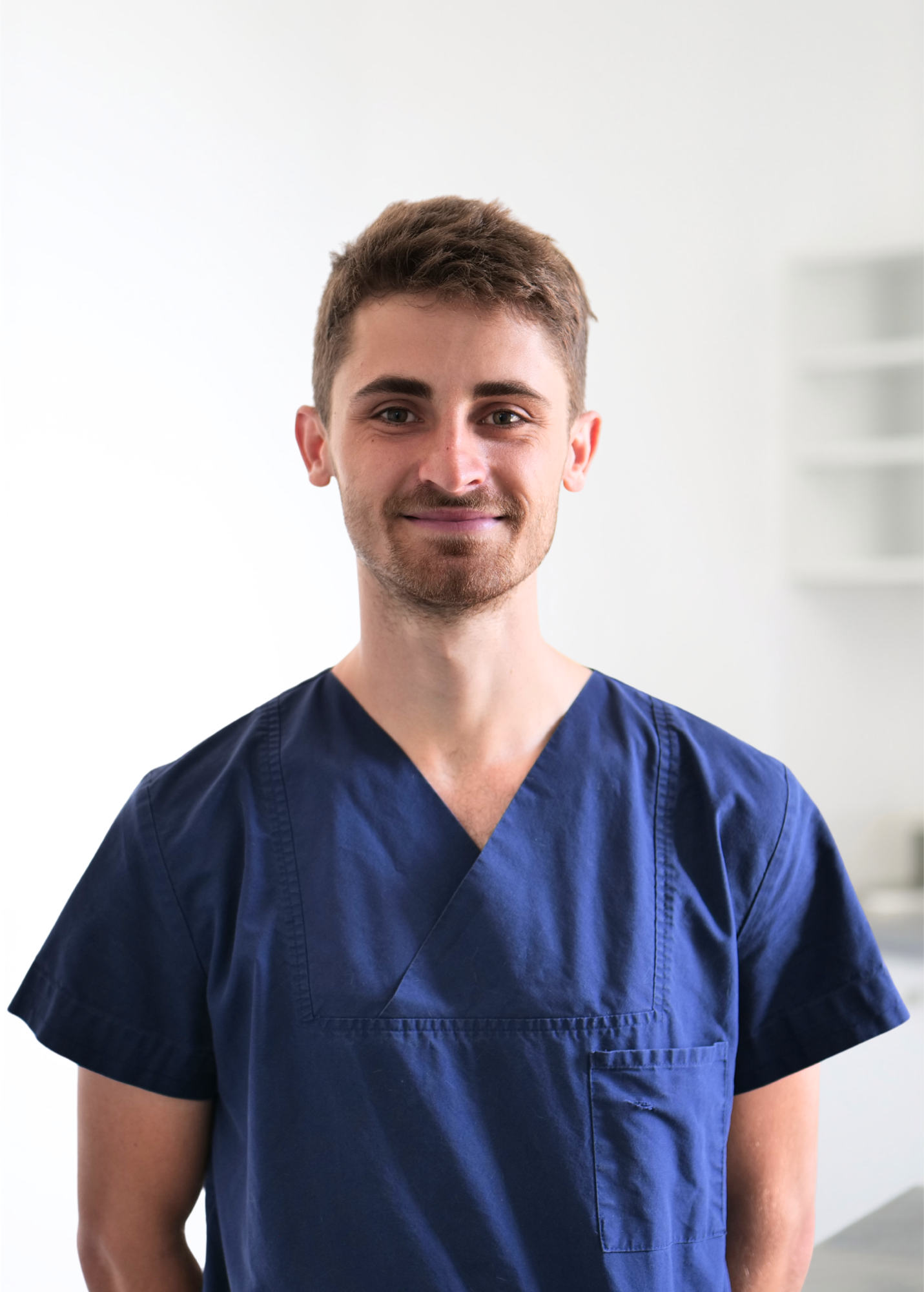 Personne debout à l'intérieur, sur fond blanc éclatant, portant une chemise bleu marine et arborant un léger sourire.