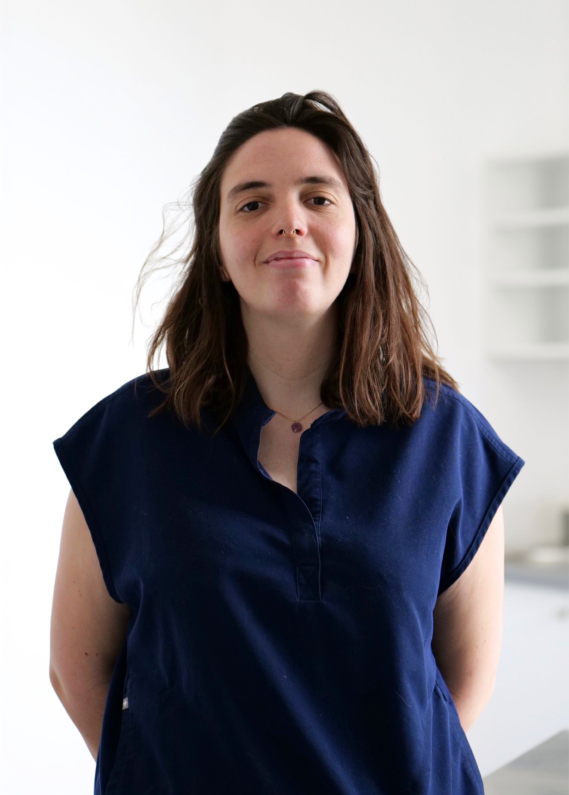 Personne debout à l'intérieur, sur fond blanc éclatant, portant une chemise bleu marine et arborant un léger sourire.