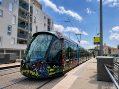 Tramway moderne et coloré sur des rails longeant des immeubles d'habitation sous un ciel bleu