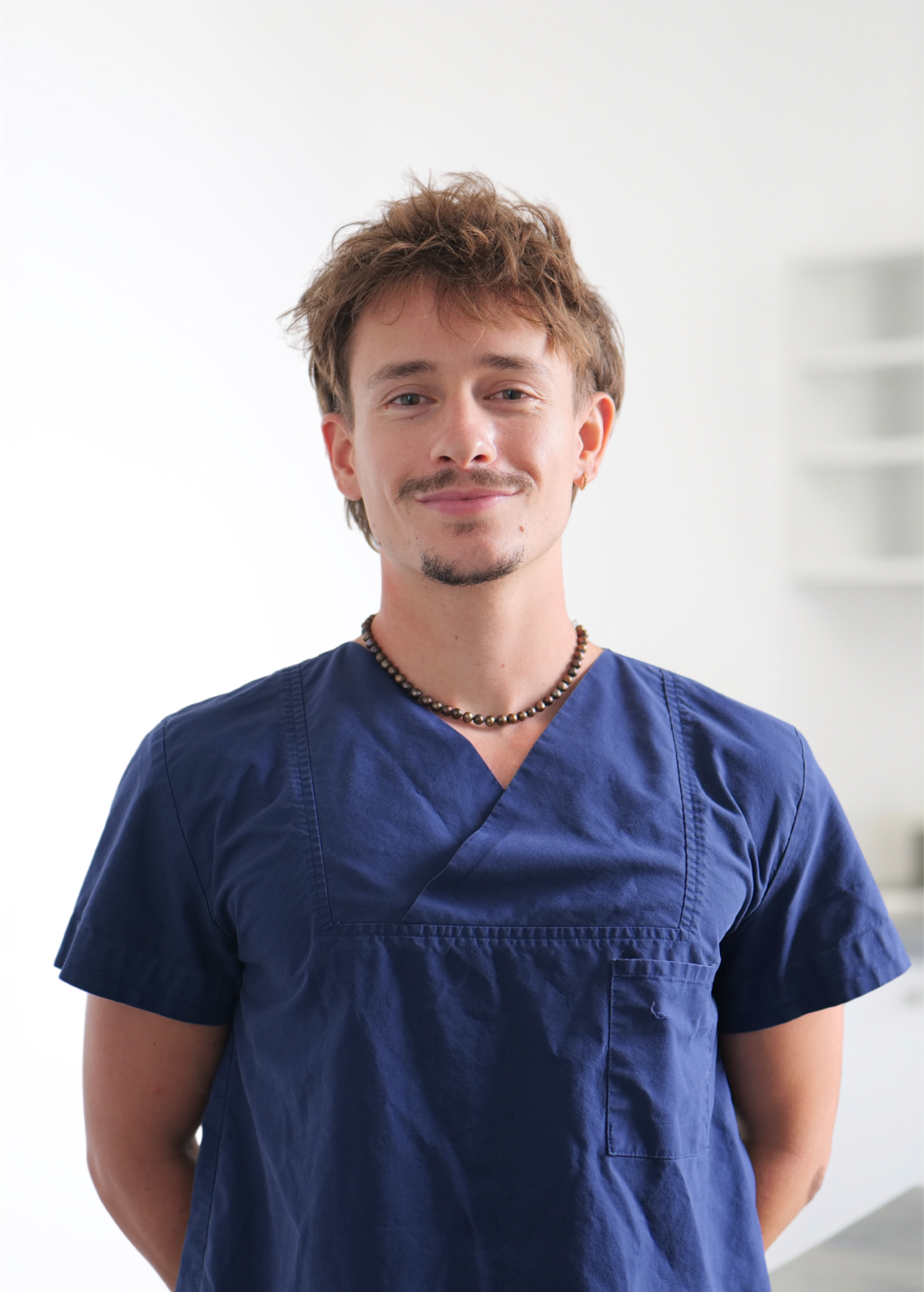 Personne souriante en blouse médicale bleu marine se détachant sur un fond blanc éclatant