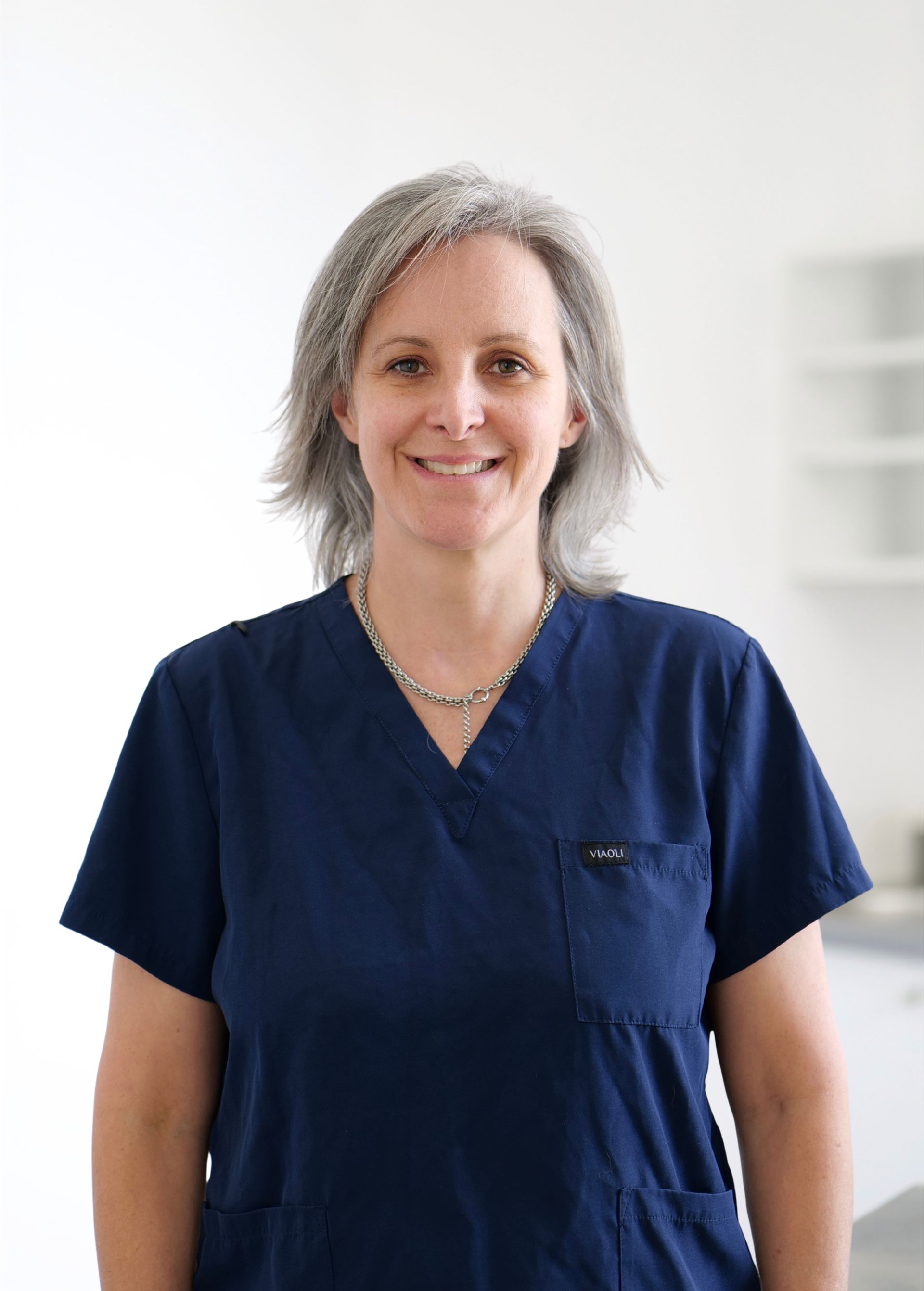 Personne souriante en blouse médicale bleu marine se détachant sur un fond blanc