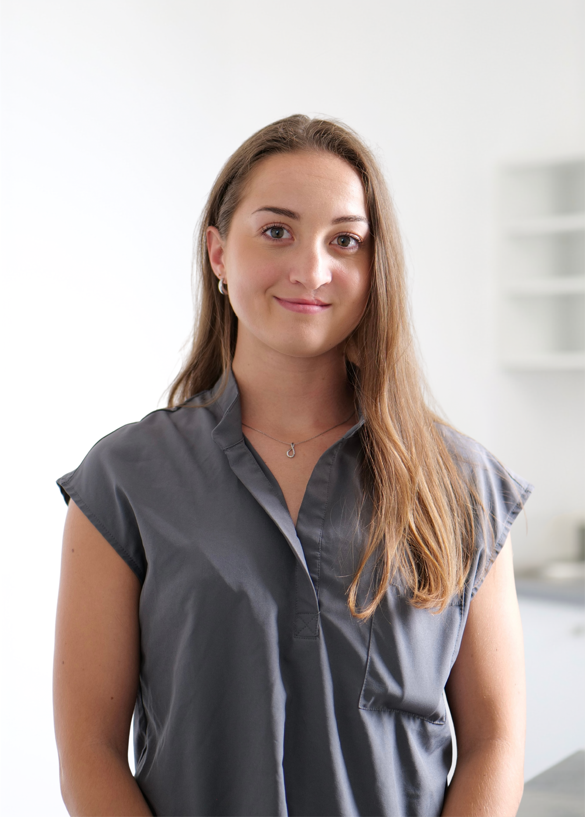Femme en chemisier gris debout à l'intérieur sur un fond blanc éclatant