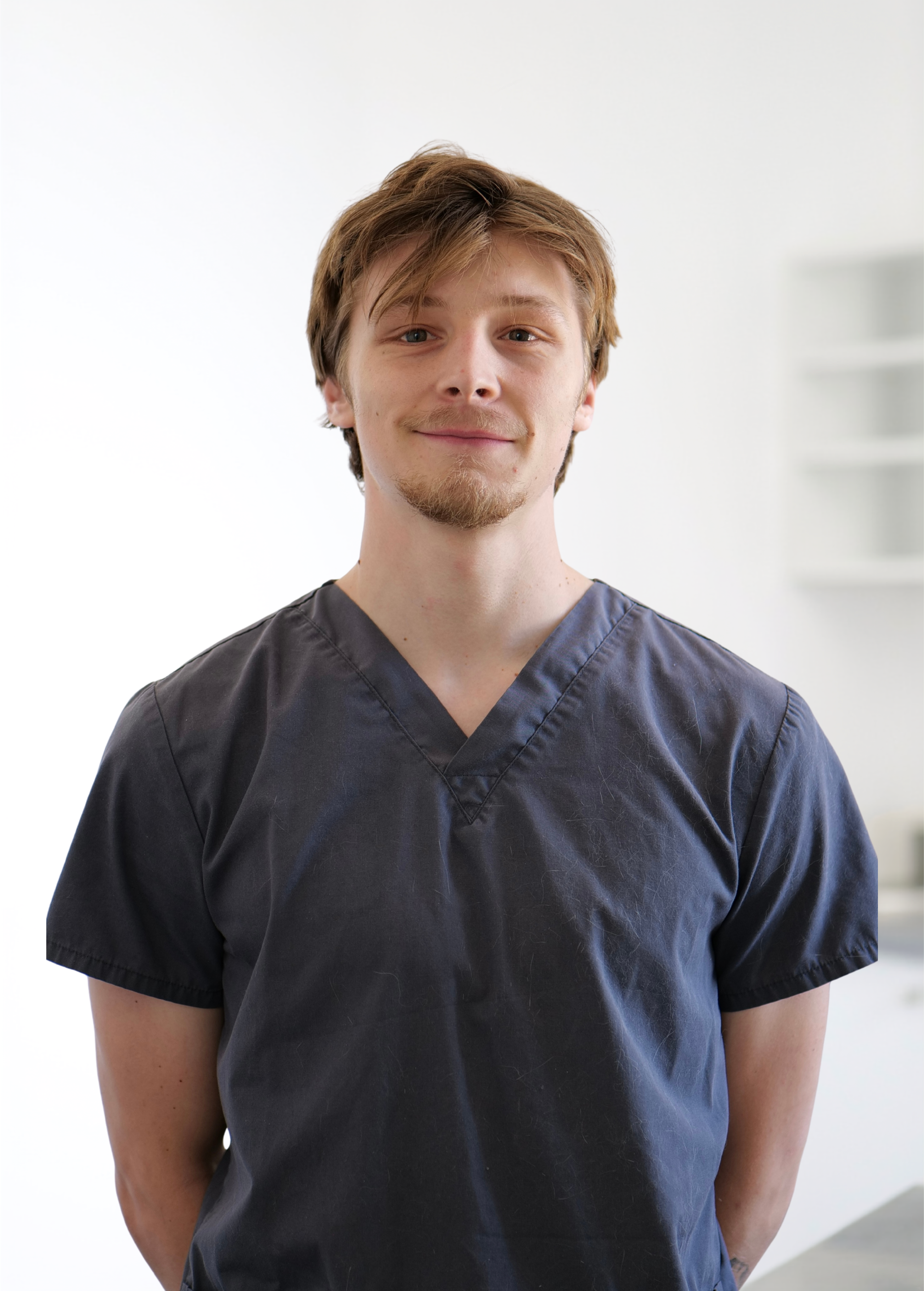 Personne en blouse médicale bleu foncé, debout à l'intérieur sur un fond clair, regardant droit devant elle.