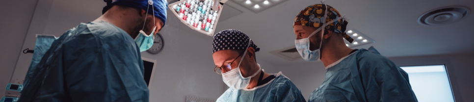 Des médecins en blouse et charlotte bleues discutent du cas d'un patient dans une salle d'opération.