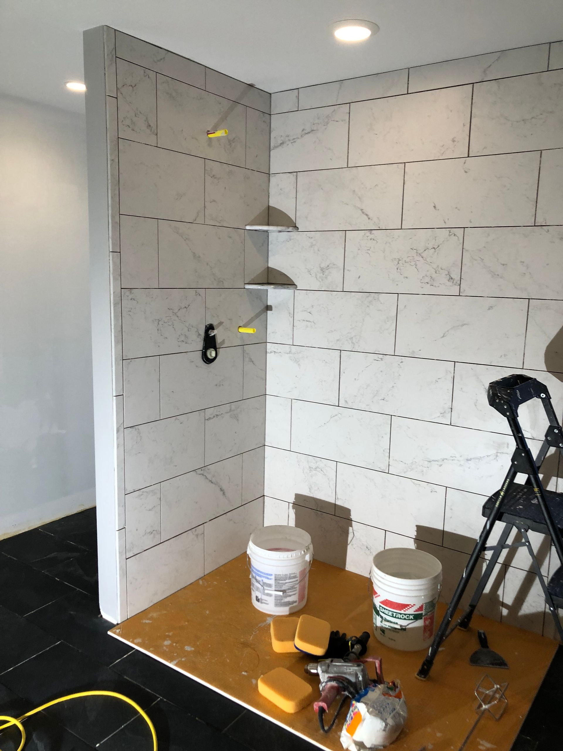 Small room with white wall tiles, paint buckets, tools, and a step ladder during renovation.