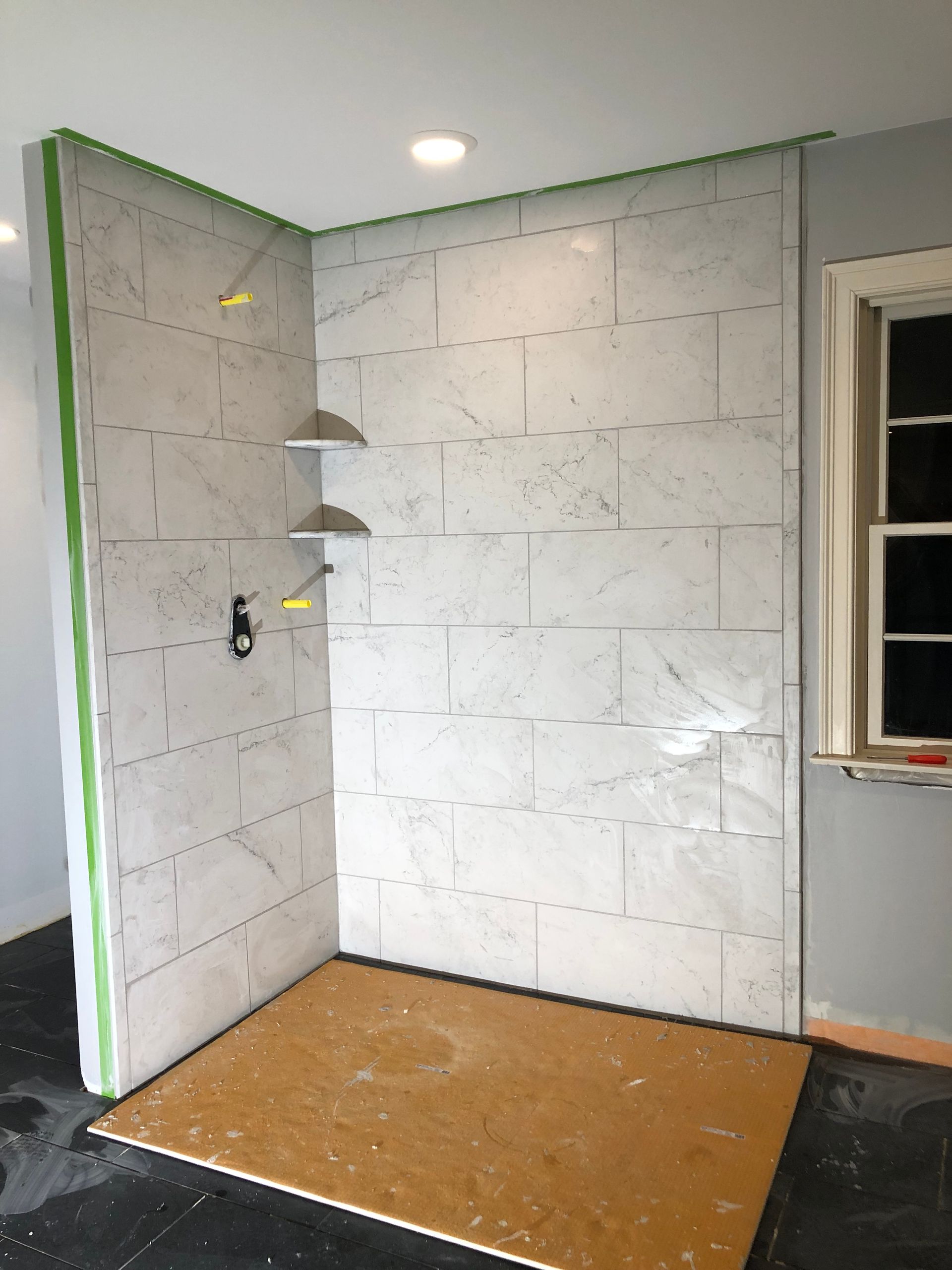 Empty small room with white cinderblock walls, gray trim, and a plywood floor panel.