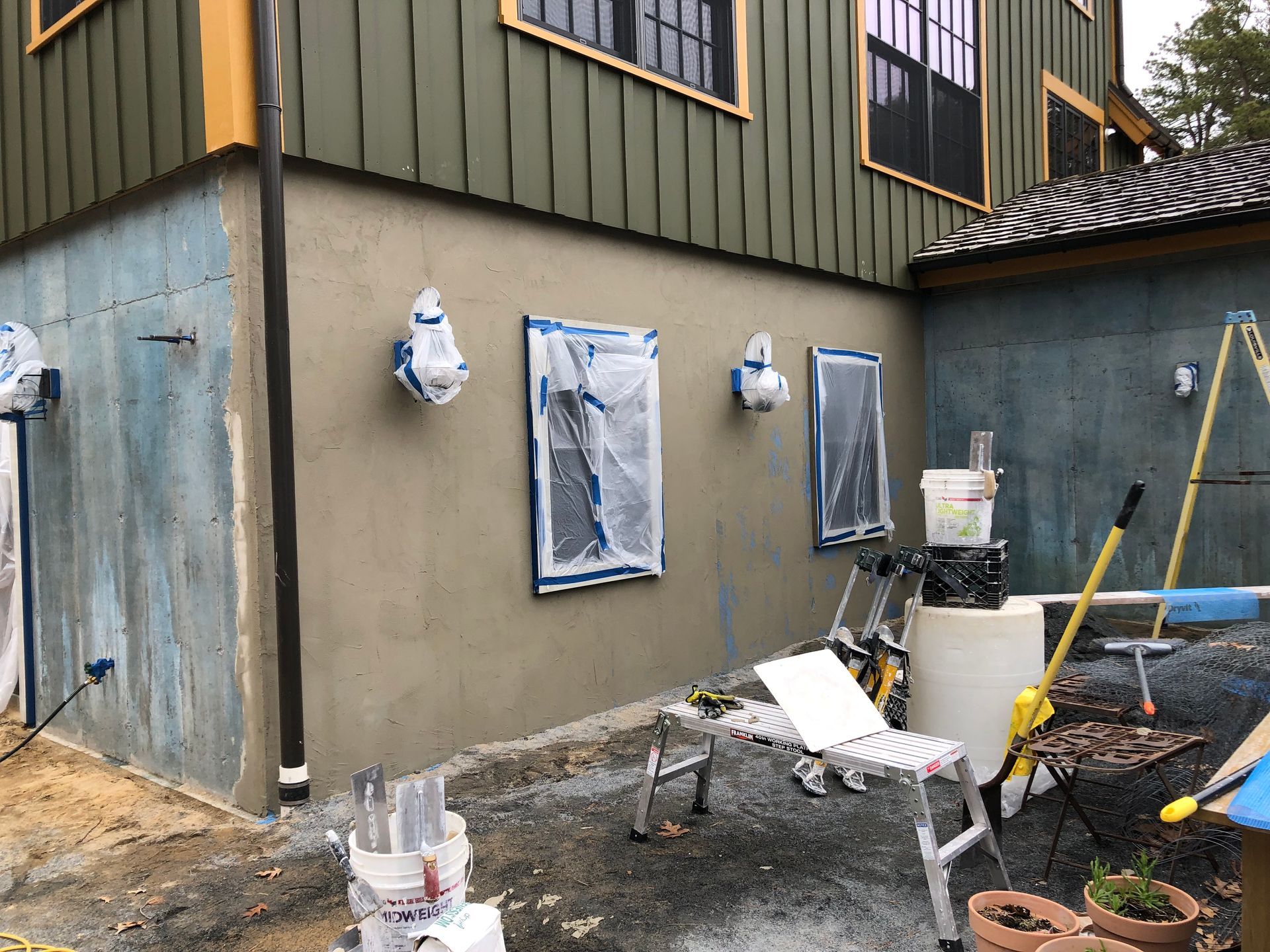 House exterior under renovation with tarped windows, tools, and construction materials in the yard