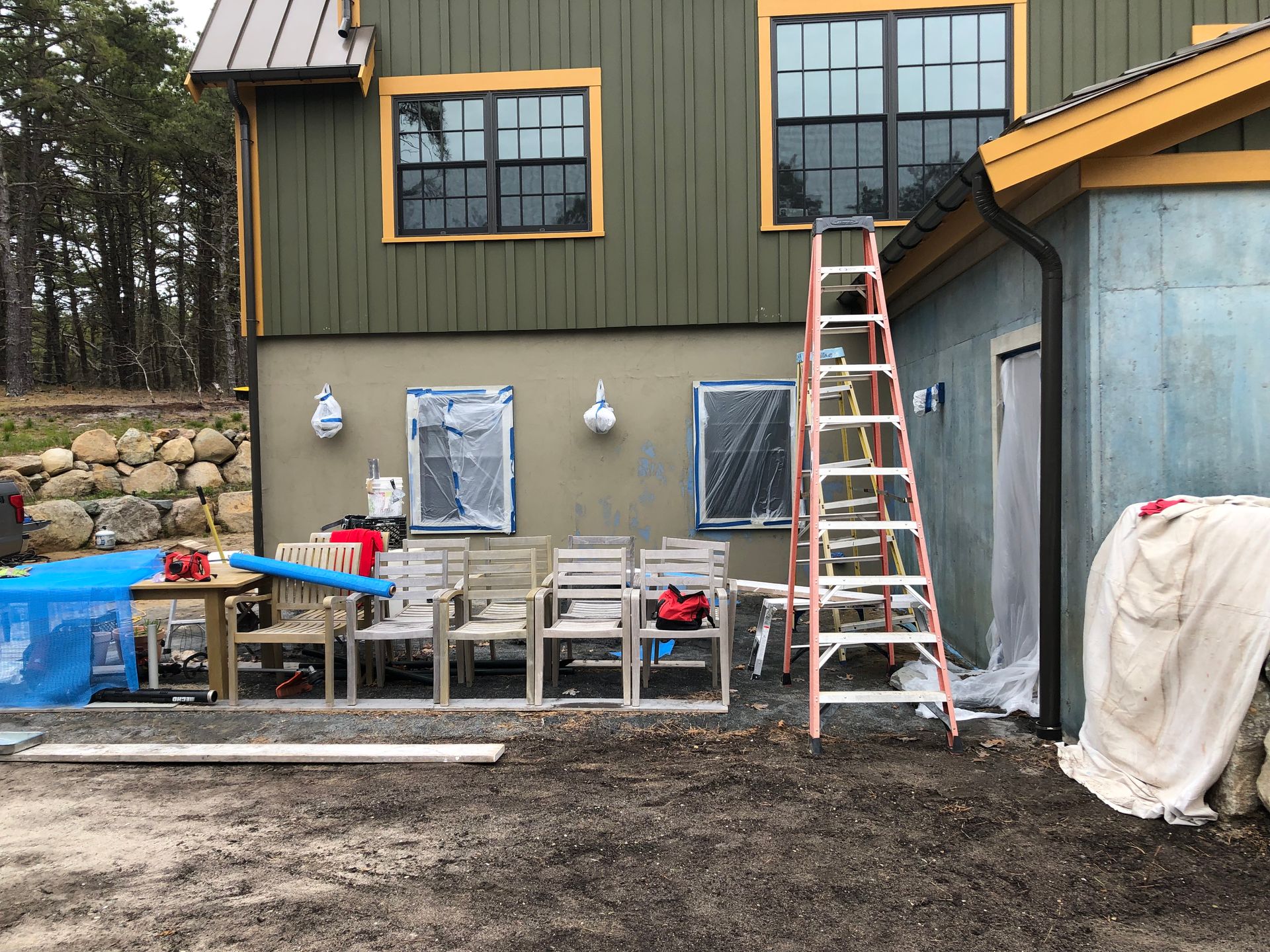 House exterior with ladder, patio furniture, and construction materials in a yard