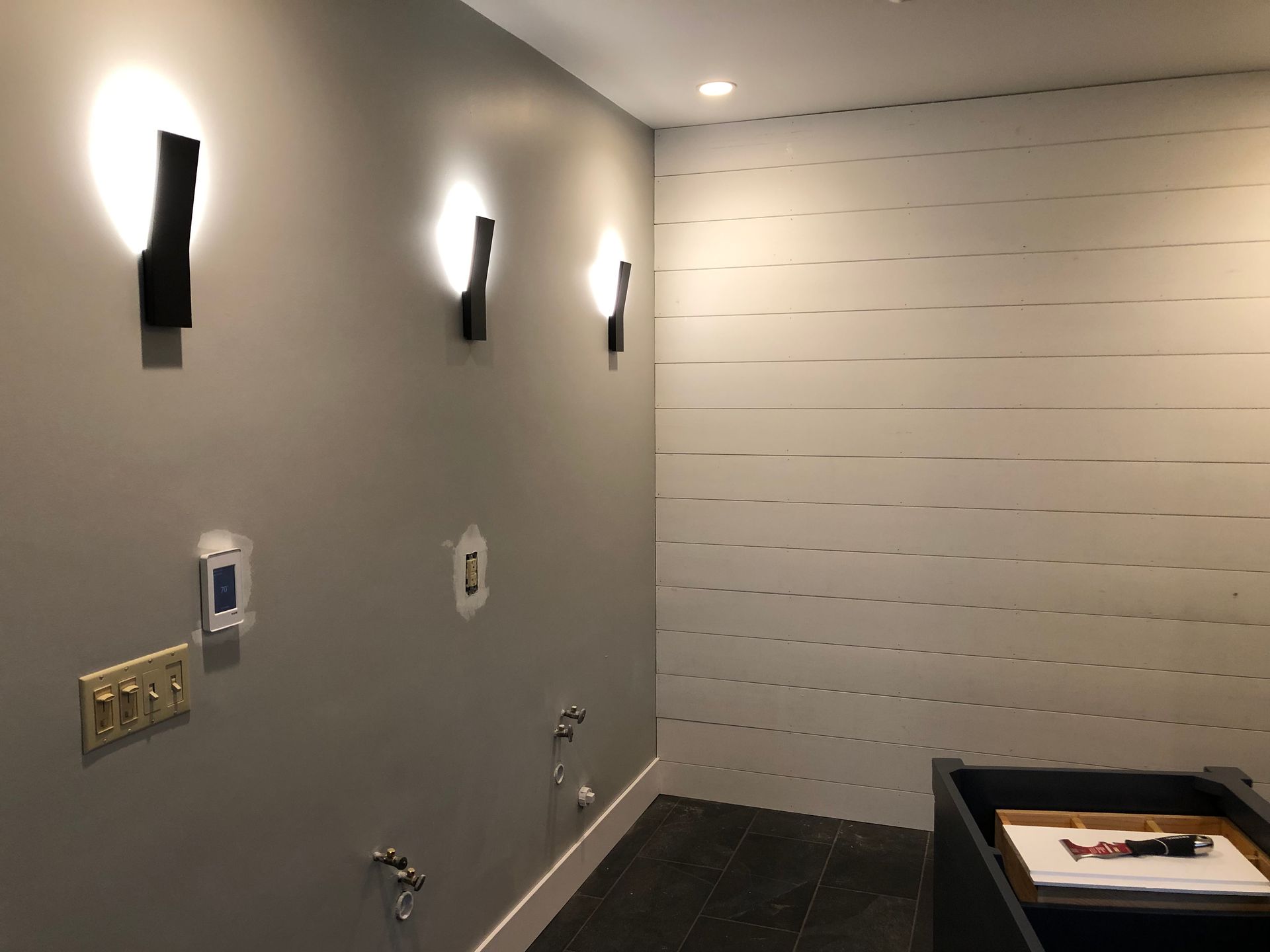 Empty modern bathroom with wall lights, gray walls, white tiled shower area, and a sink counter
