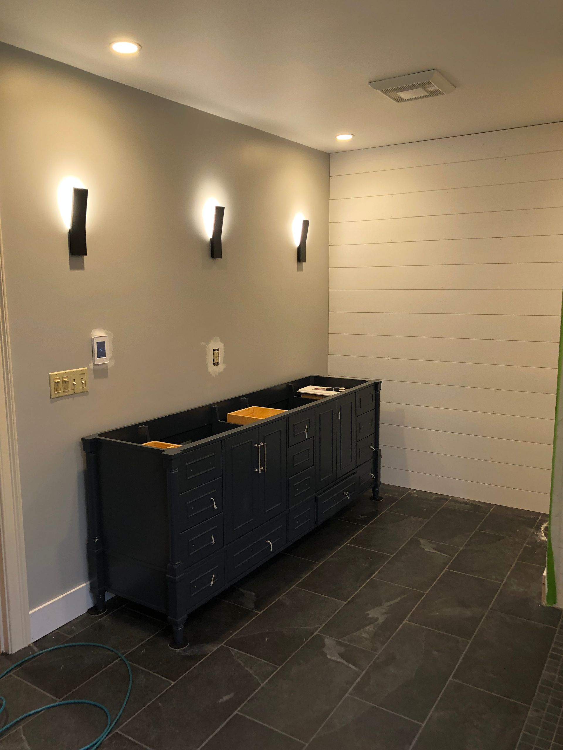 Modern restroom with gray walls, black tile floor, wall lights, and a black cabinet against a white accent wall