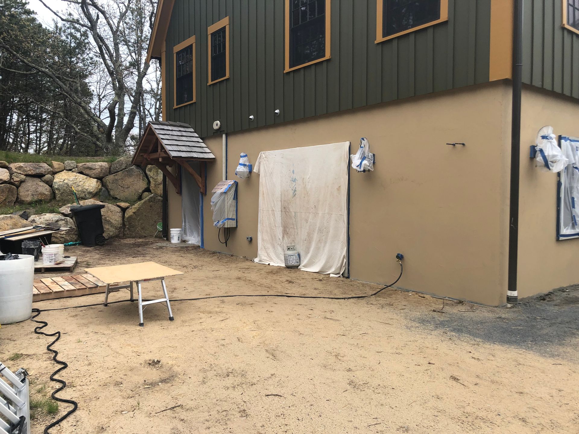 House exterior under renovation with tarps, tools, and a dirt yard
