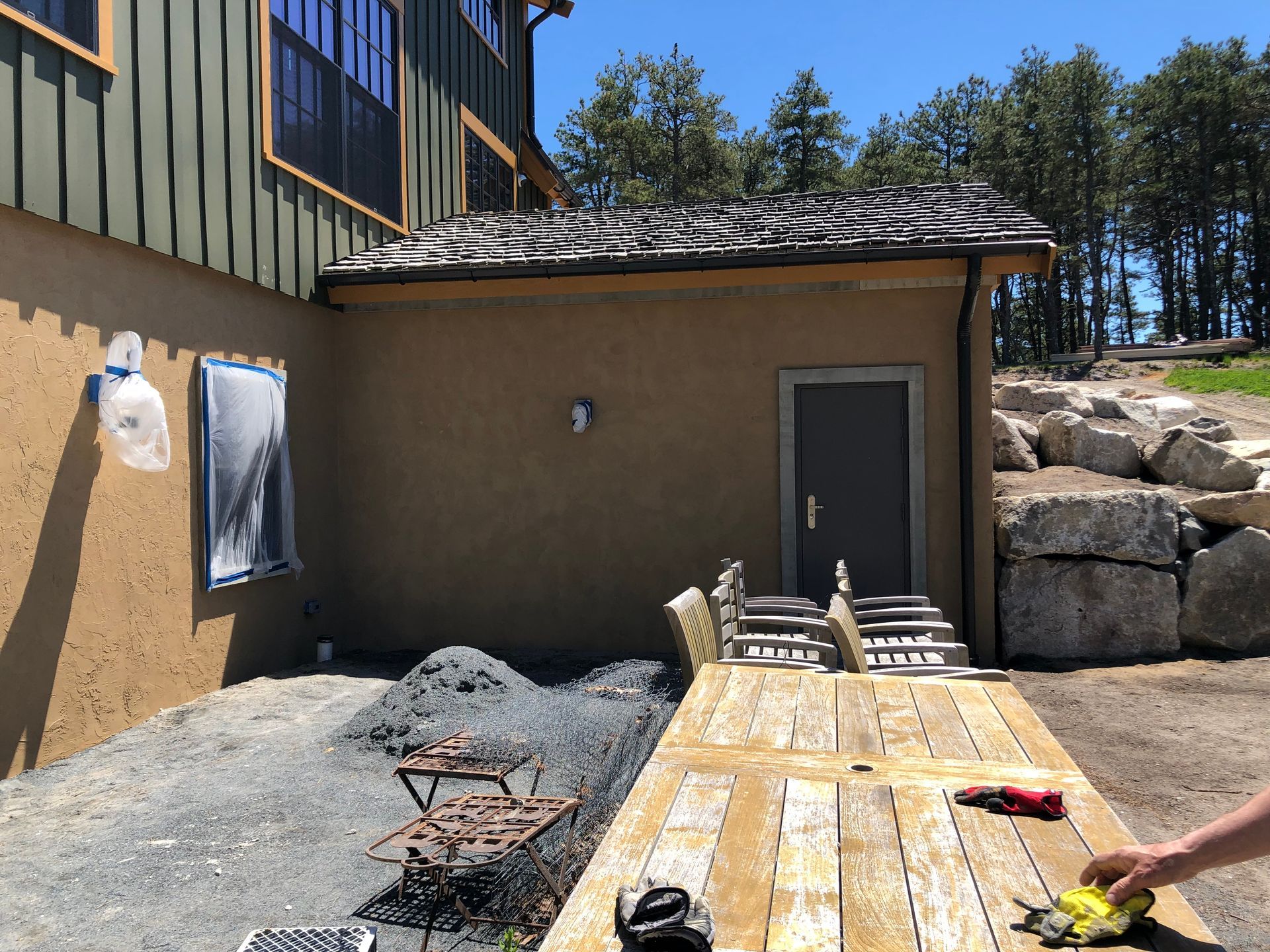 Outdoor construction area with a wooden deck, stucco building, and gravel yard under a clear sky