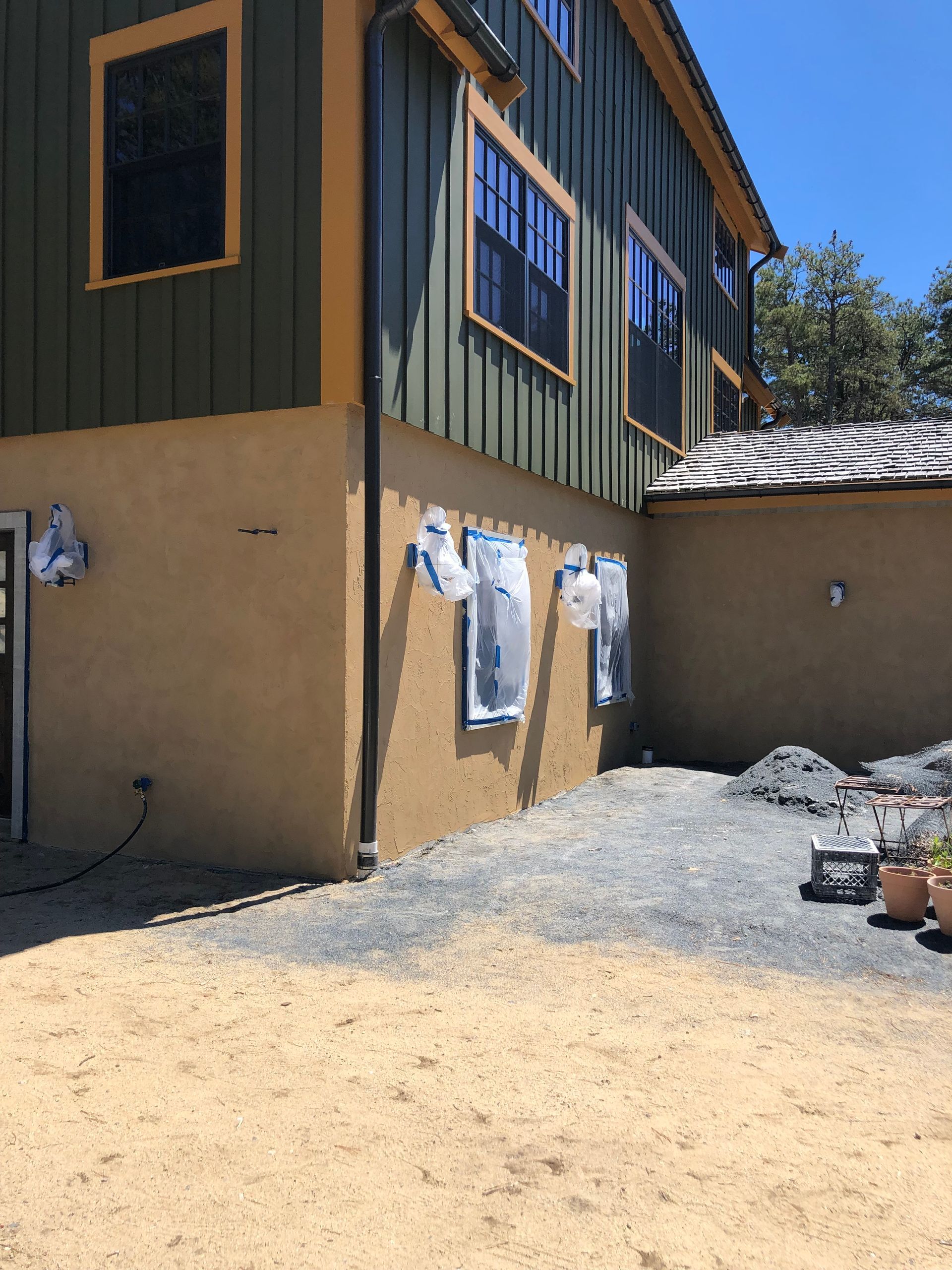 Side of a tan-and-green house with laundry hanging outside on a sunny gravel yard
