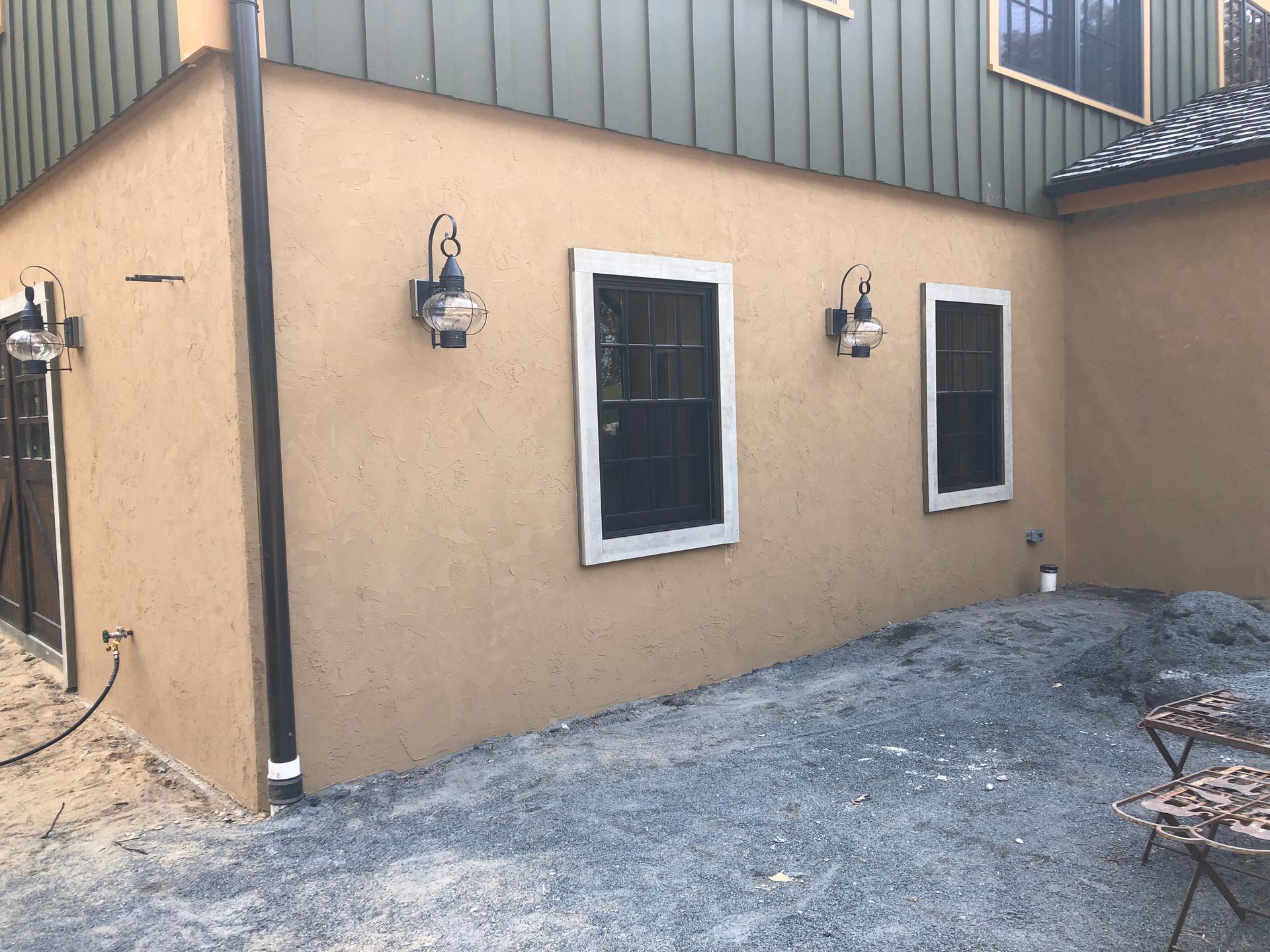 Outdoor patio beside tan stucco house with two windows, wall lanterns, and gravel ground