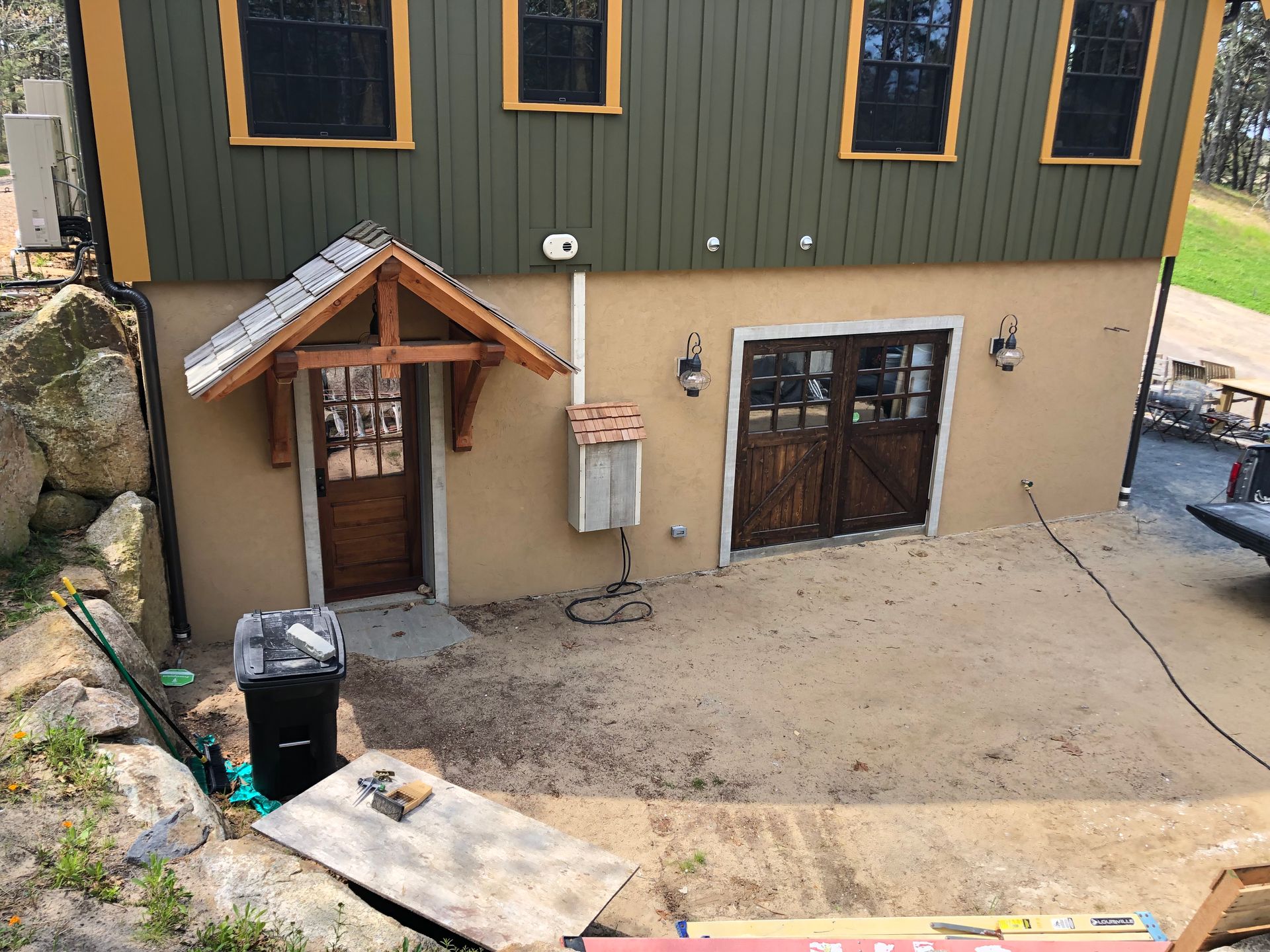 Exterior of a house with green siding, tan lower wall, small porch, and gravel courtyard
