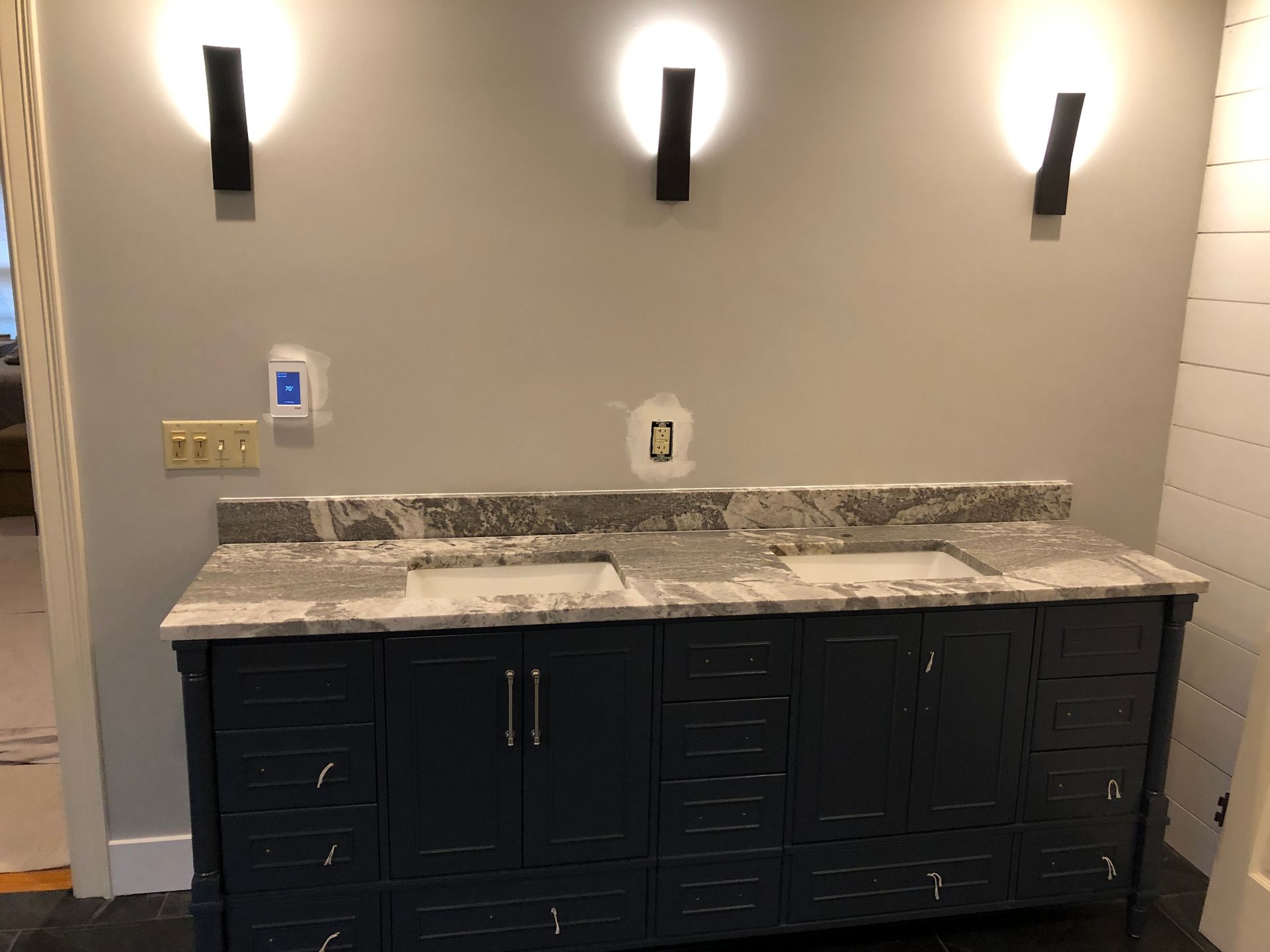 Modern bathroom vanity with black cabinets, marble countertop, and three wall sconces