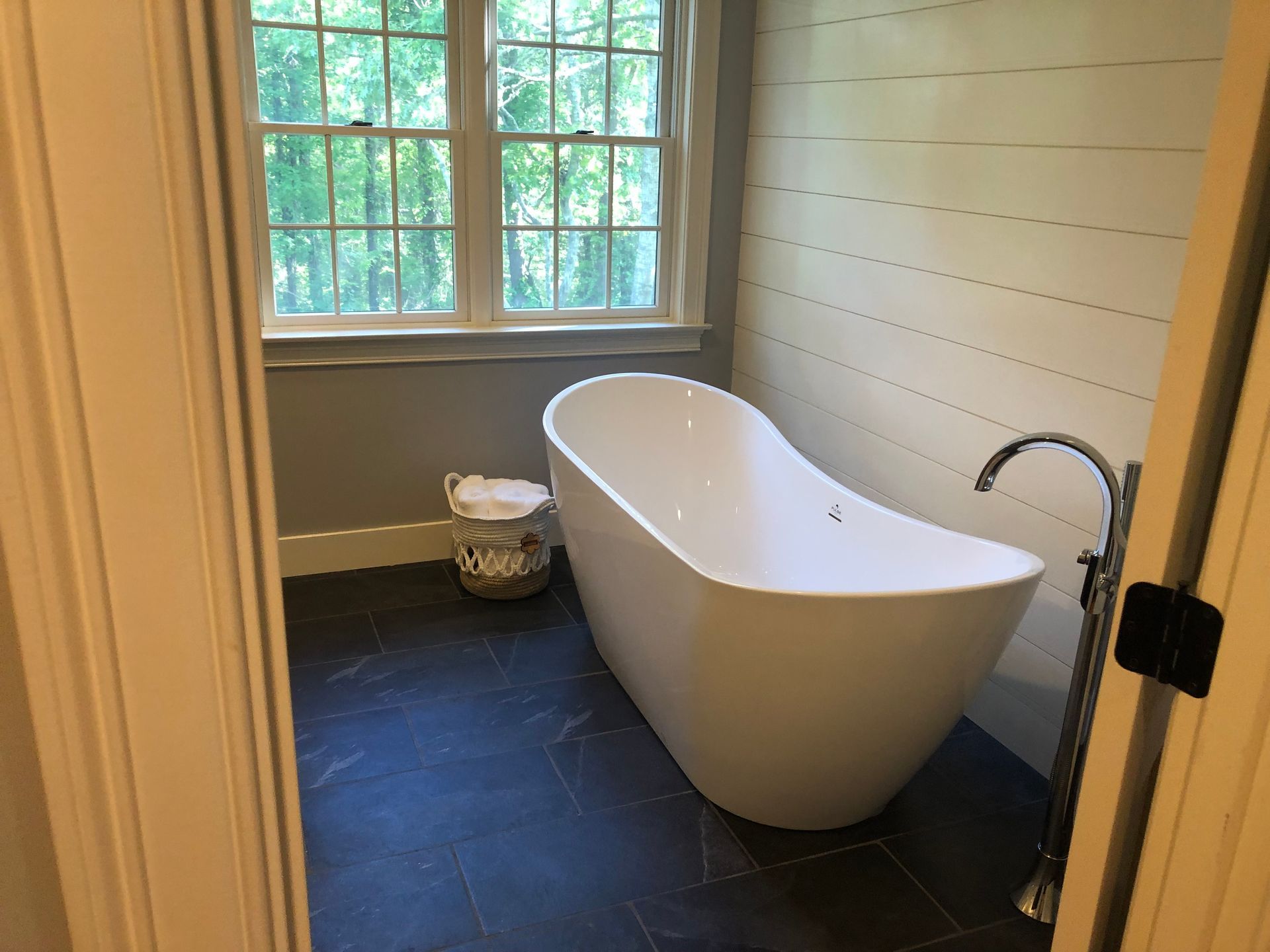 Modern bathroom with a freestanding white bathtub, window, and dark floor tiles