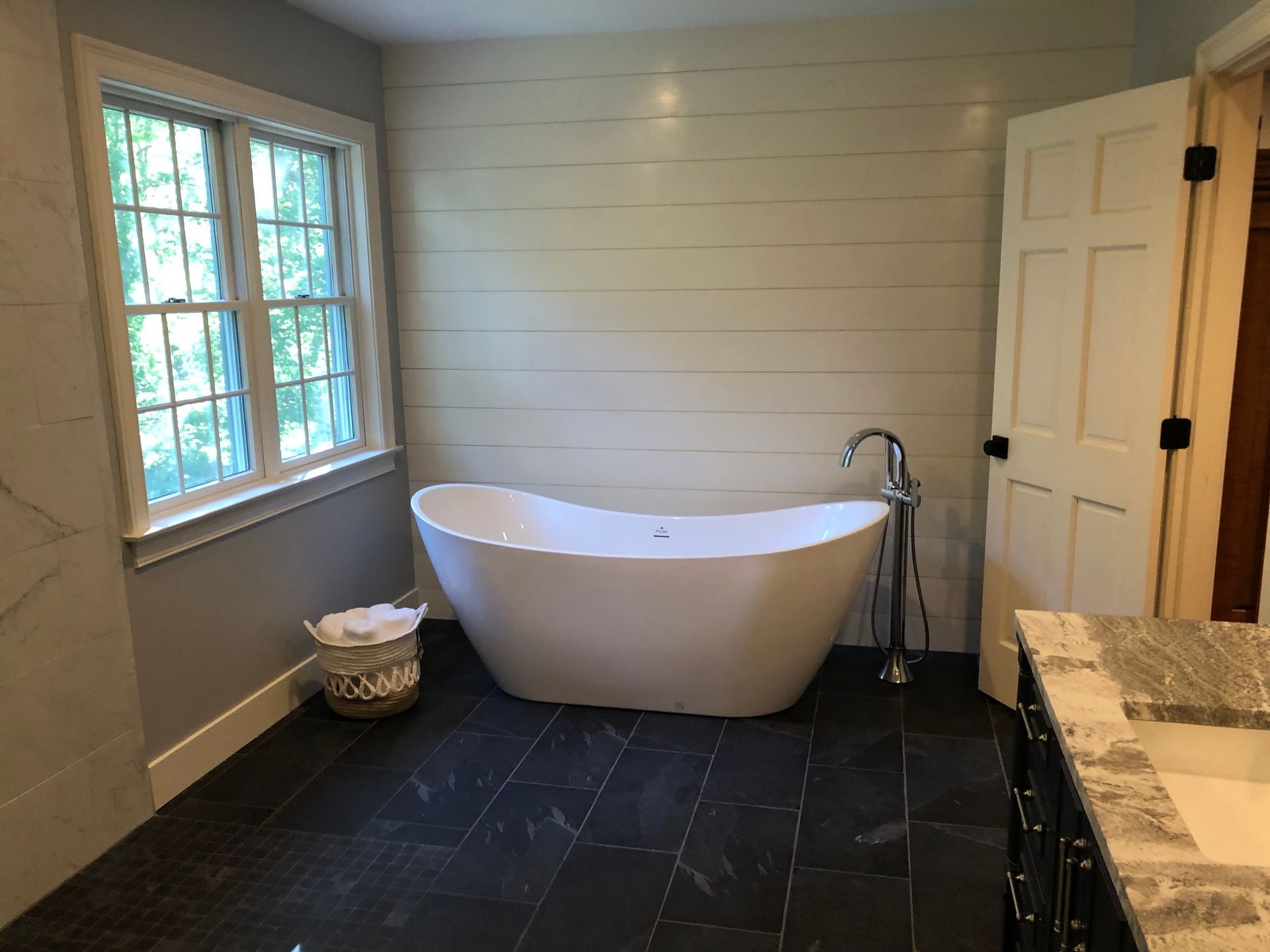 Bathroom with freestanding white tub, dark floor, window, and beige vanity.