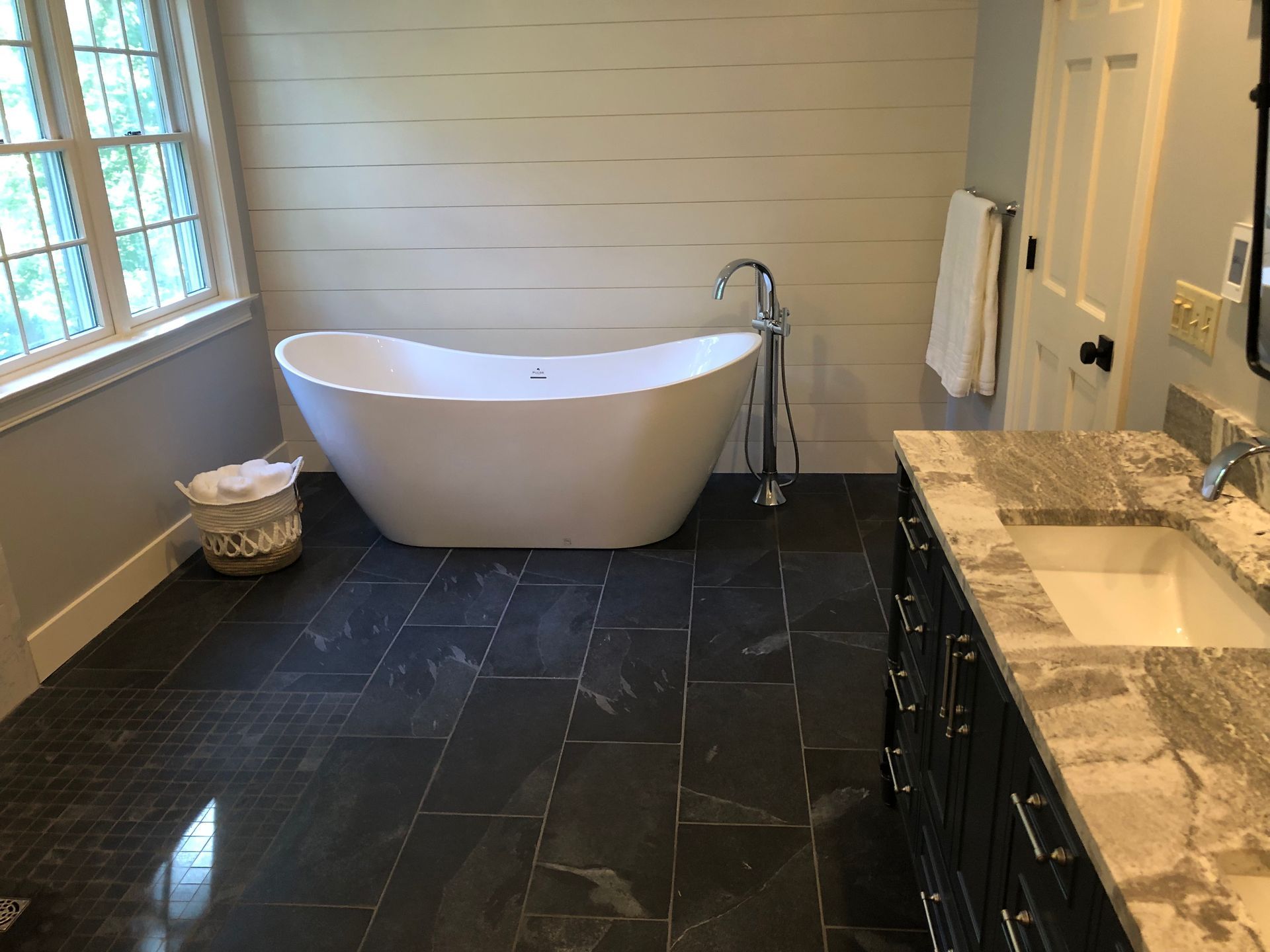 Modern bathroom with freestanding white tub, dark tile floor, and double vanity sink.