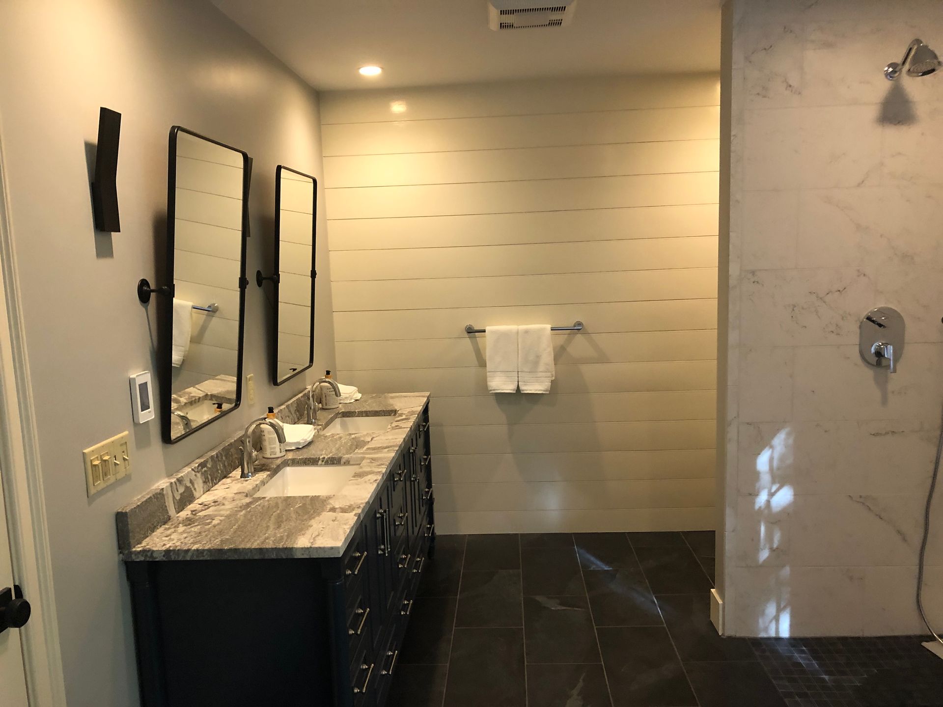 Modern bathroom with double vanity, wall mirrors, and marble shower tile with towel bar