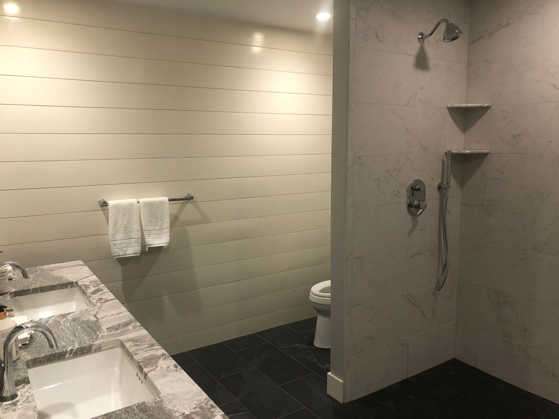 Modern bathroom with marble vanity, towel rack, and tiled shower stall with shelves.