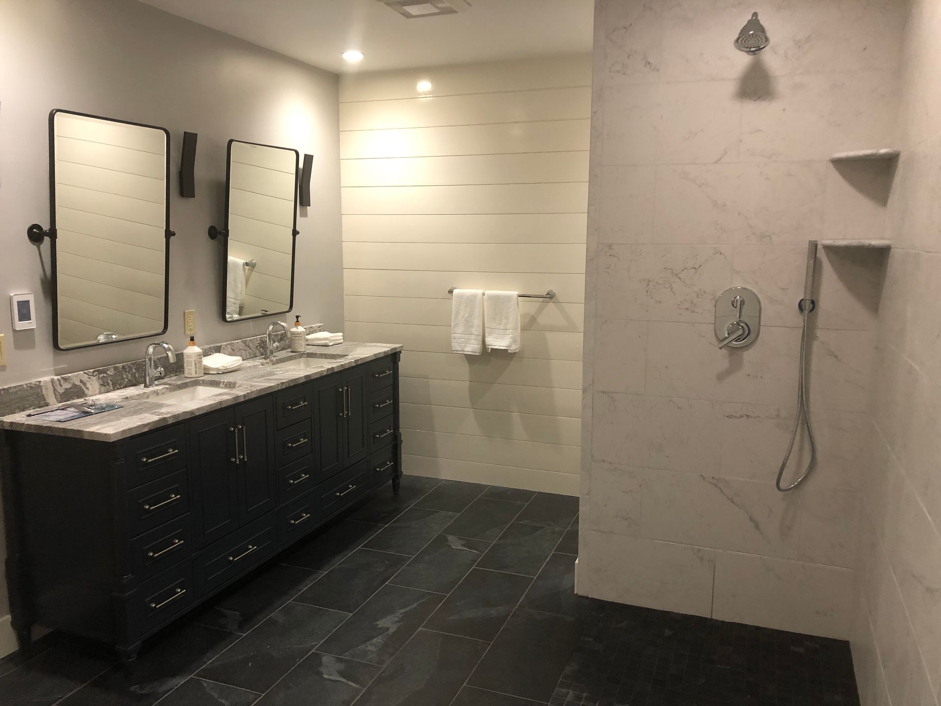 Modern bathroom with double vanity, mirrors, and tiled shower area in gray tones