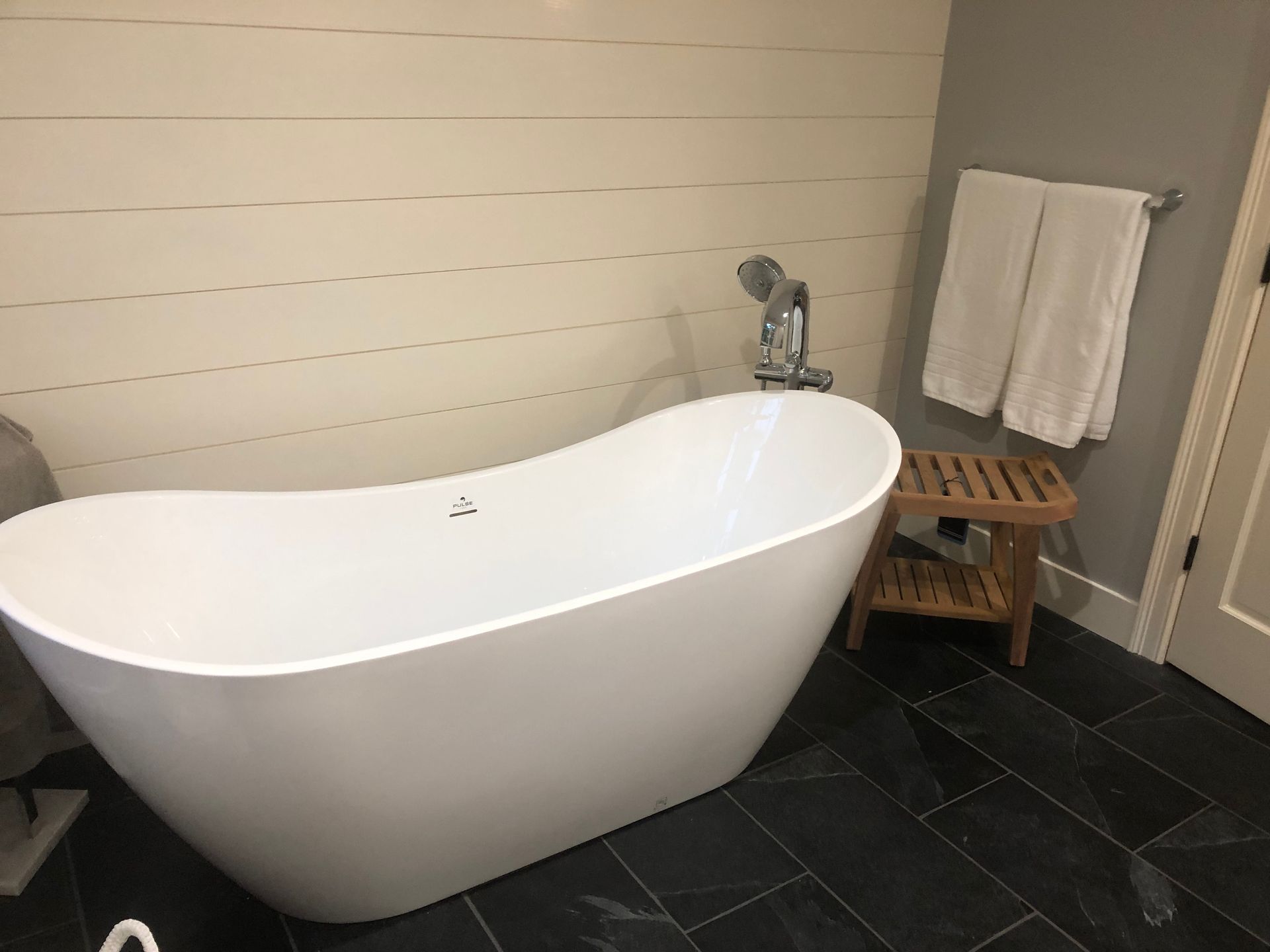 White freestanding bathtub in a modern bathroom with dark tile floor and towel rack