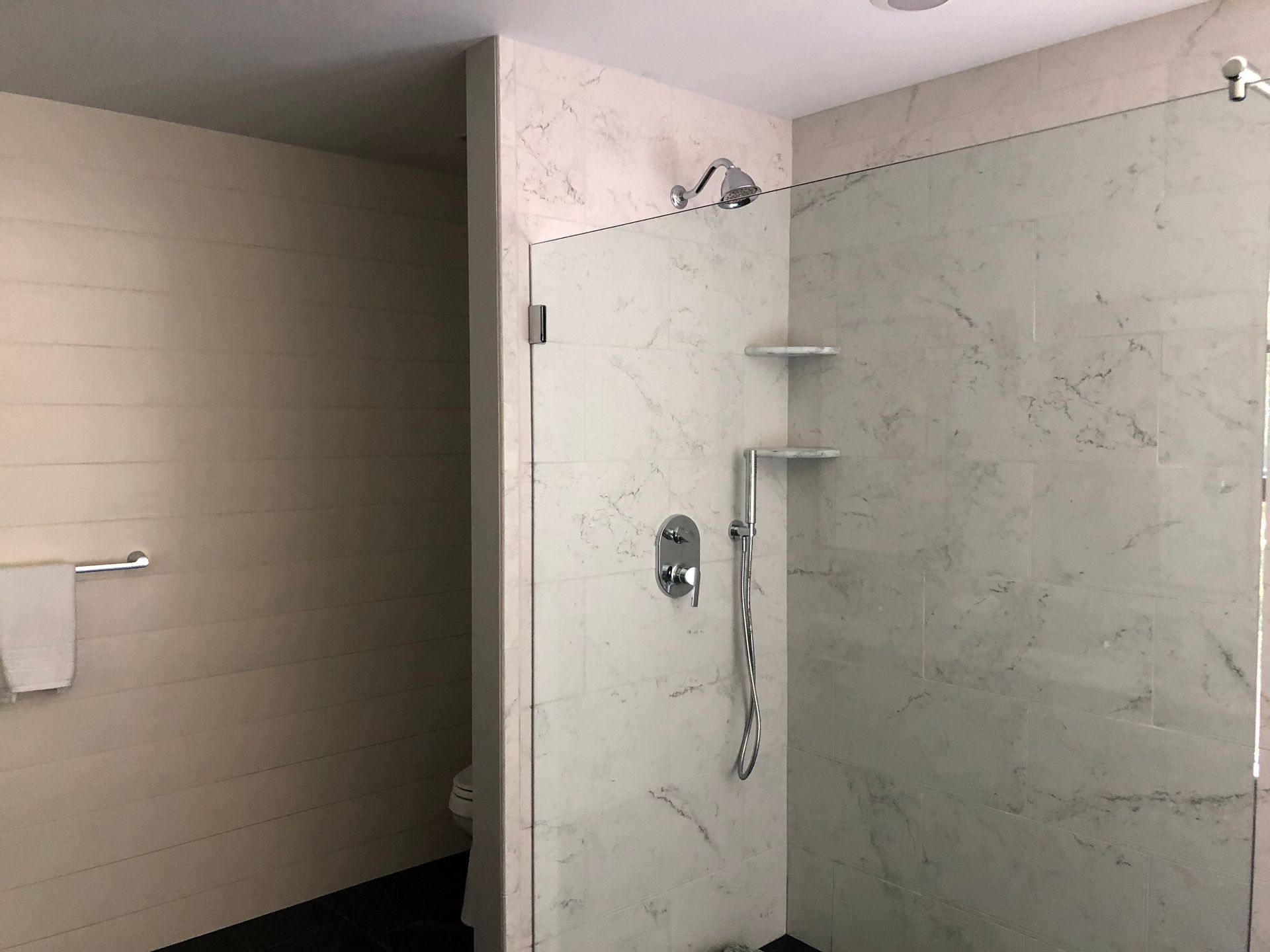 Bathroom shower with glass door, chrome fixtures, and beige tile walls