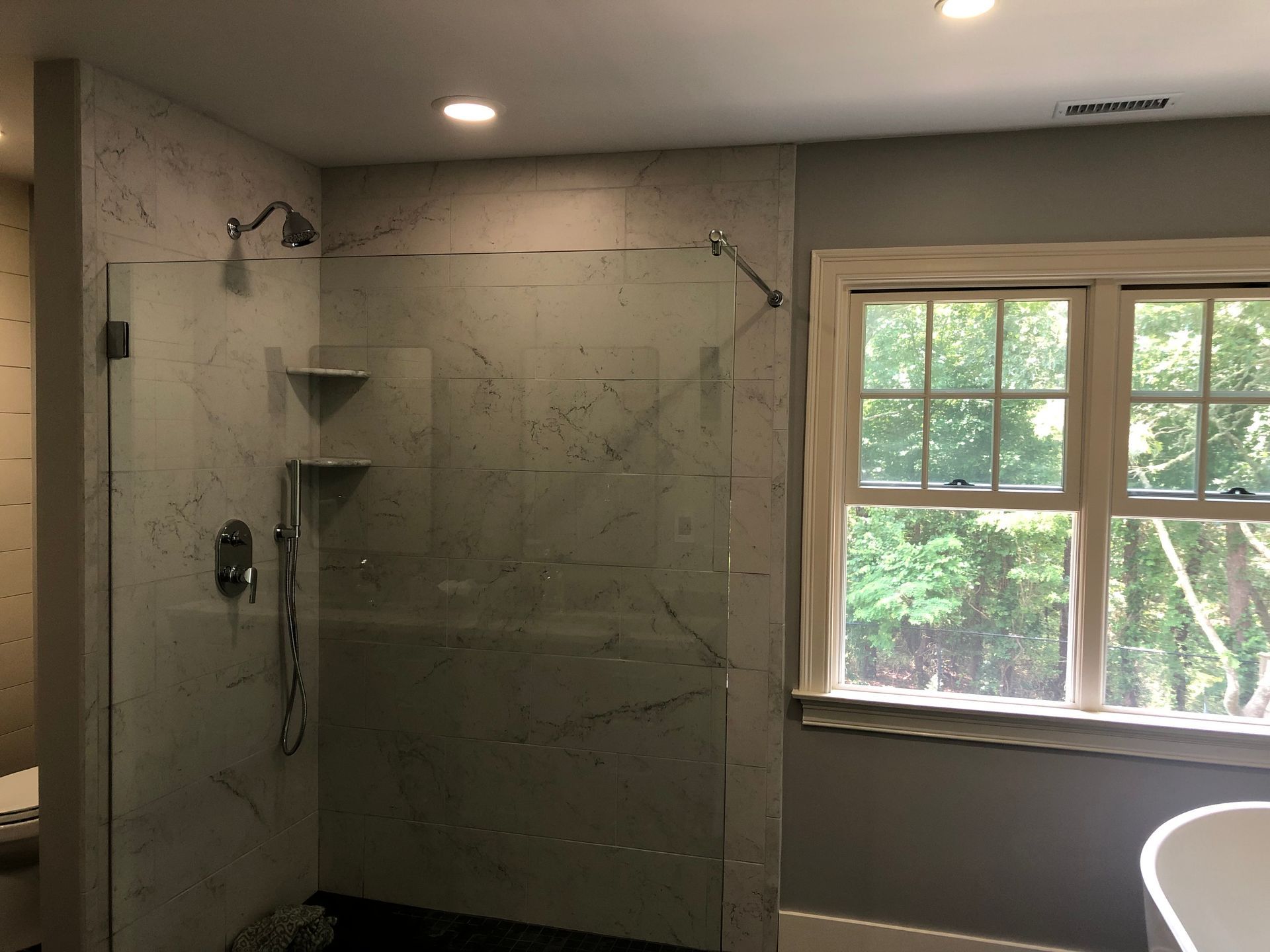 Modern bathroom with glass shower enclosure, recessed lights, and a window above a bathtub
