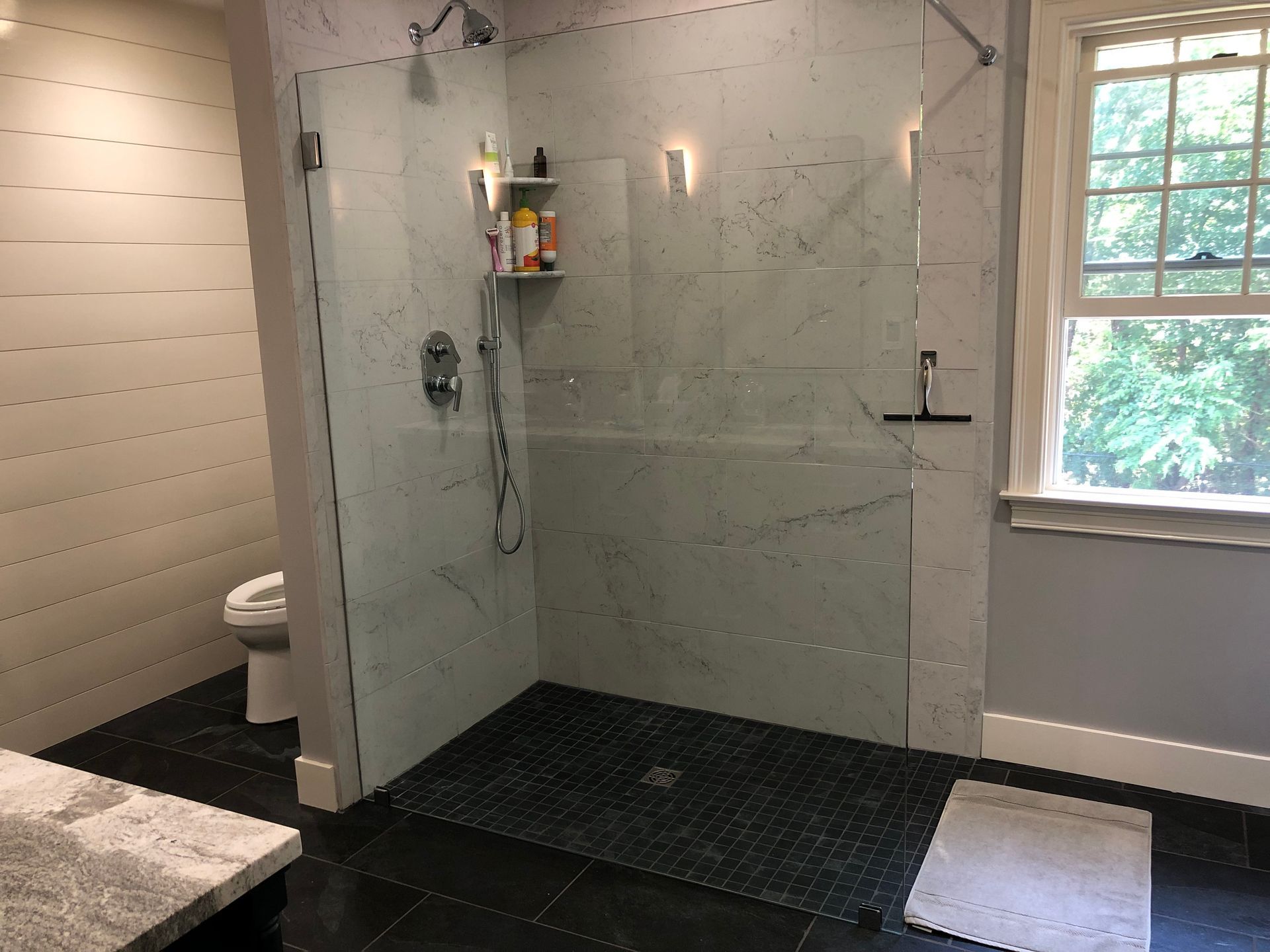 Modern bathroom shower with glass partition, tiled walls, black floor, and window light